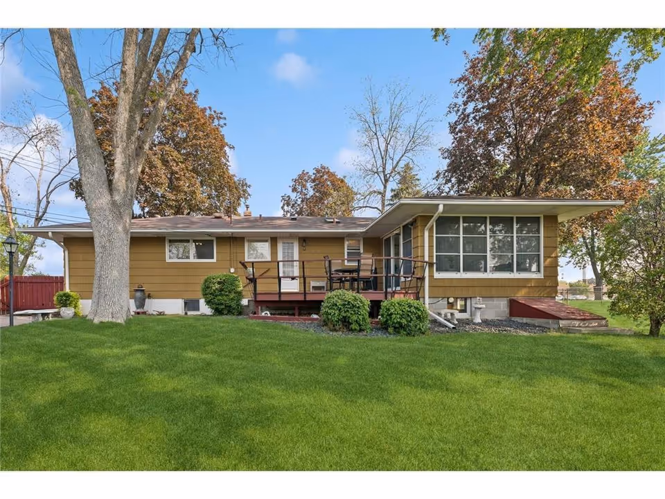 Single-story yellow building with a front deck, green lawn, and surrounding trees.