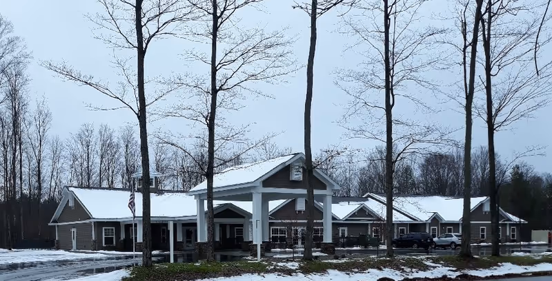 Snowy exterior view of August Haus Assisted Living with a covered entrance and parked cars.