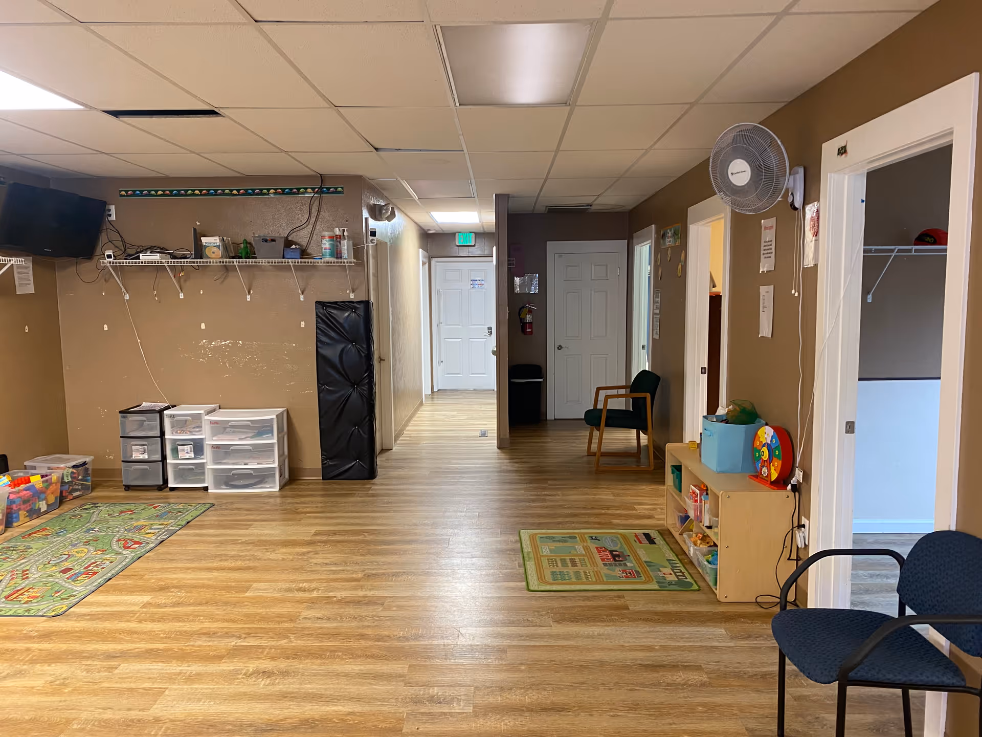 Interior common area with wood floors, toys, shelves, chairs, and a doorway to a hallway.