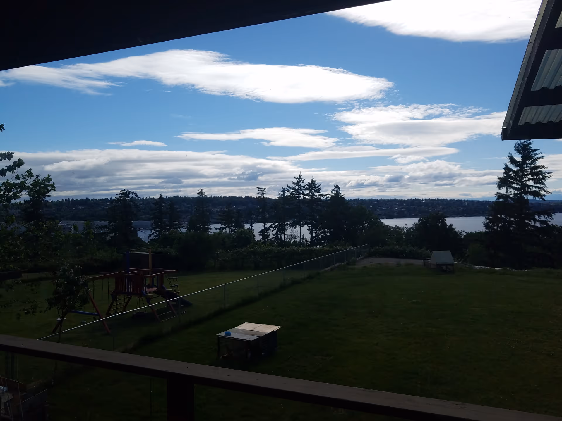 Balcony view of a grassy yard with a playground, trees, and a lake in the distance.