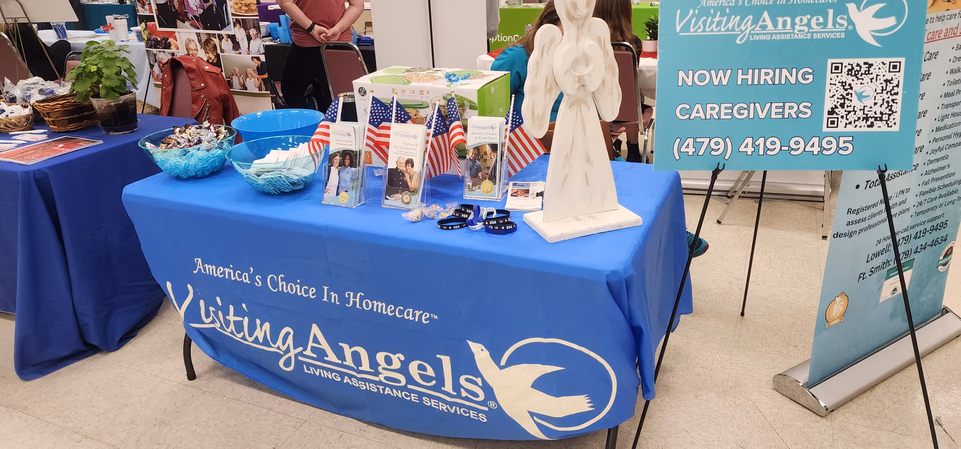 Blue Visiting Angels booth table with brochures and an angel statue.