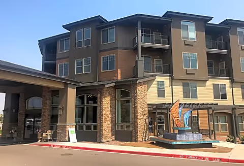 Three-story senior living building exterior with stone accents and a covered entrance.