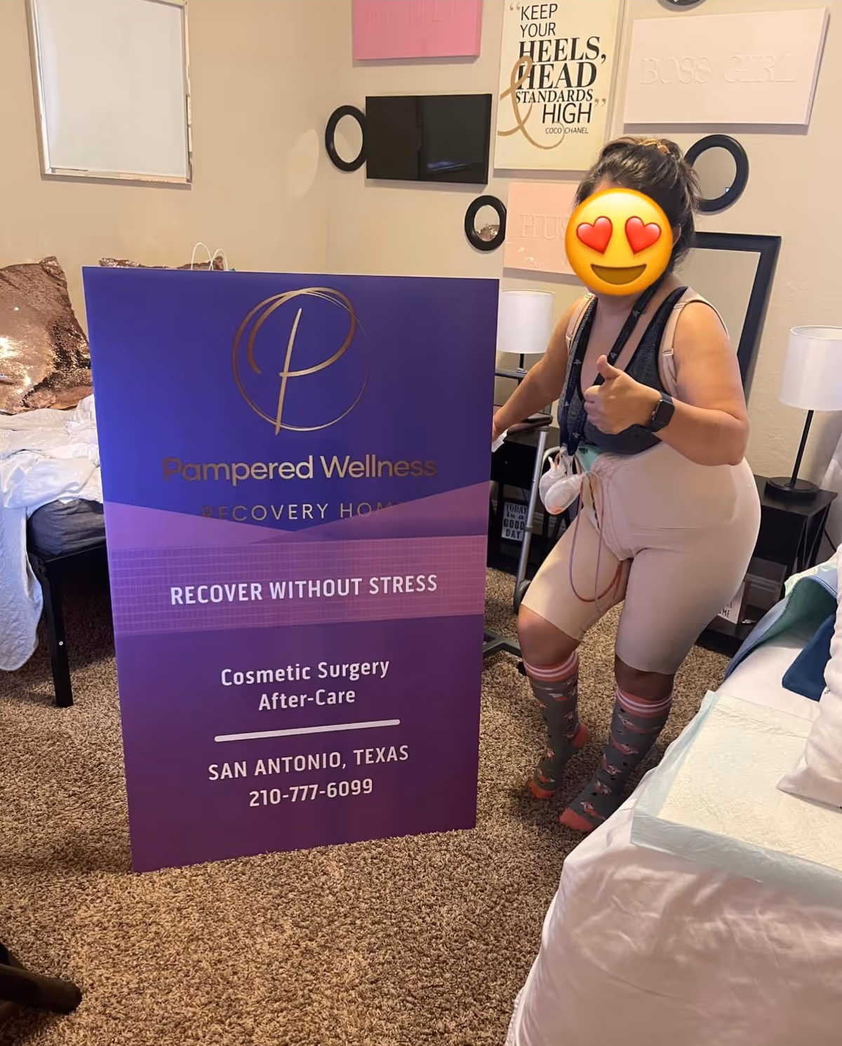 A person stands beside a purple Pampered Wellness sign inside a bedroom.