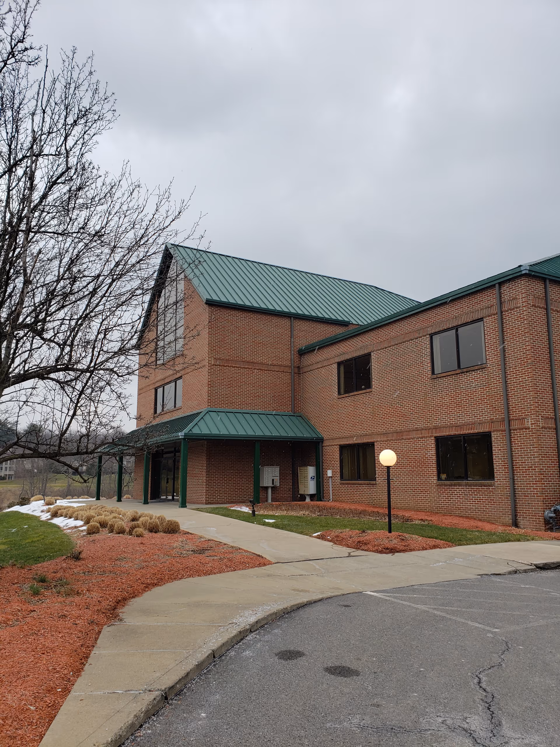 Brick senior living facility exterior with green metal roof and a covered entrance.