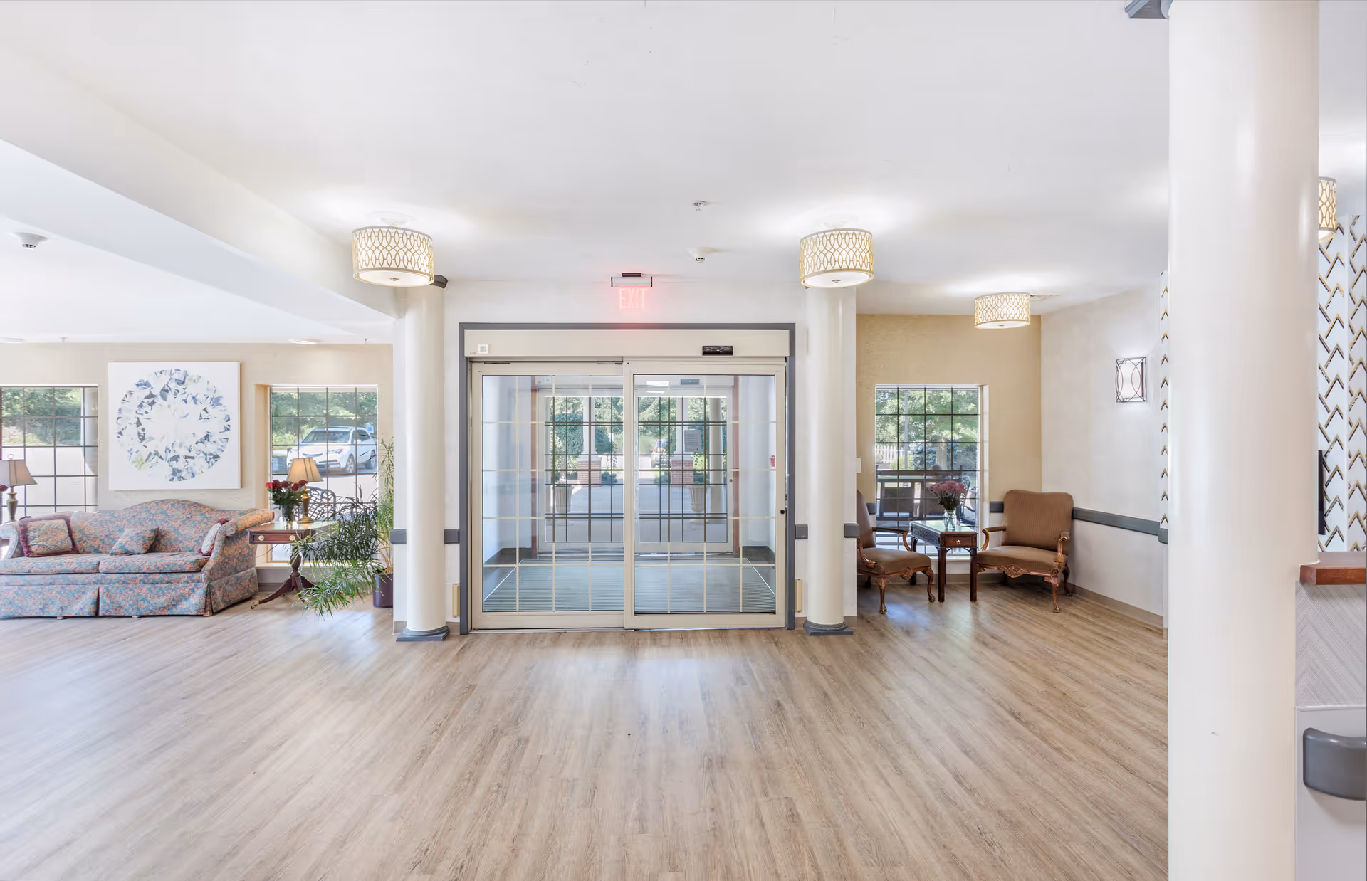 Bright lobby with double glass entrance doors, seating areas, columns and wood-look flooring.