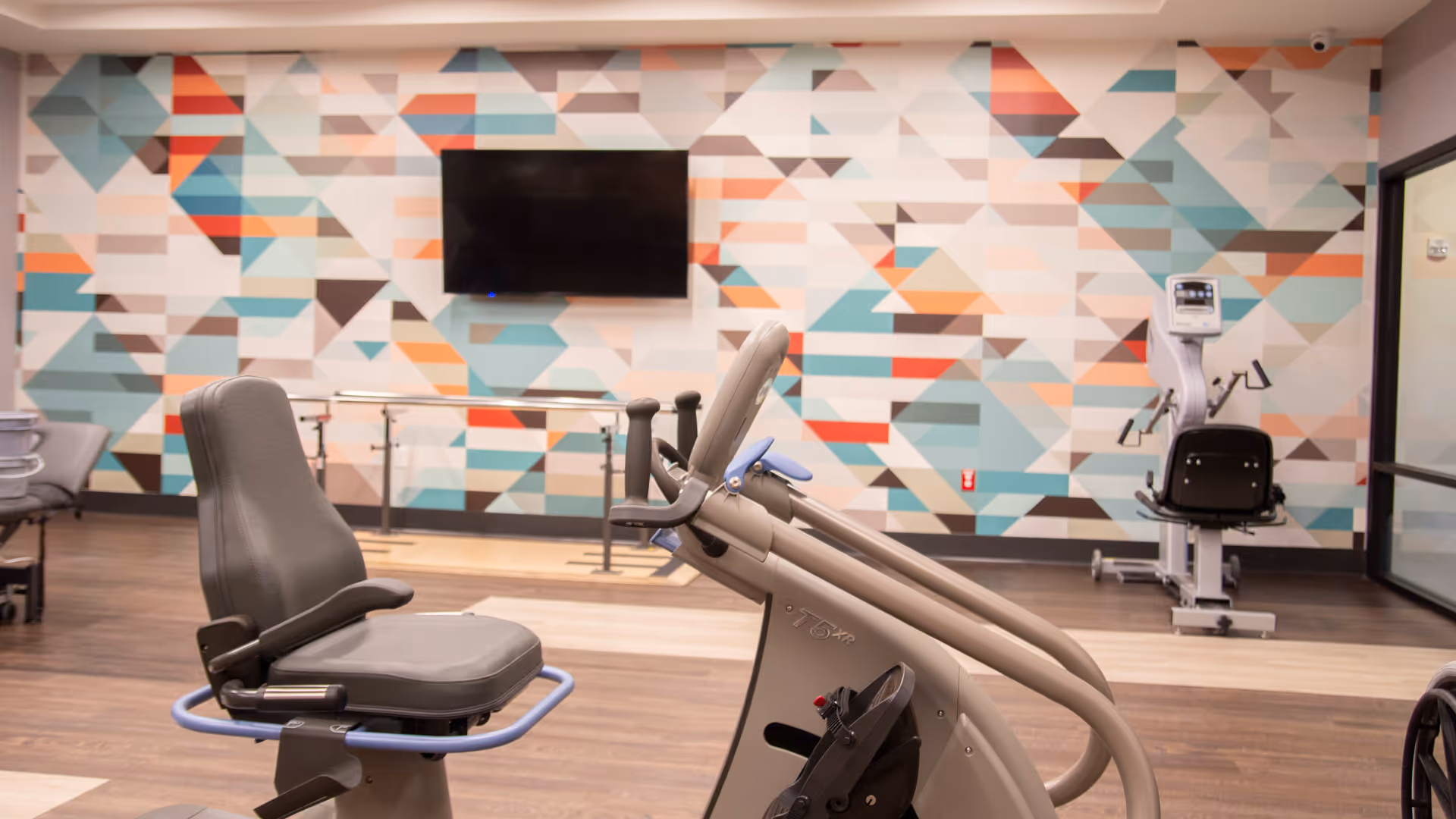 Indoor rehab gym with a stationary bike and colorful geometric wall art.