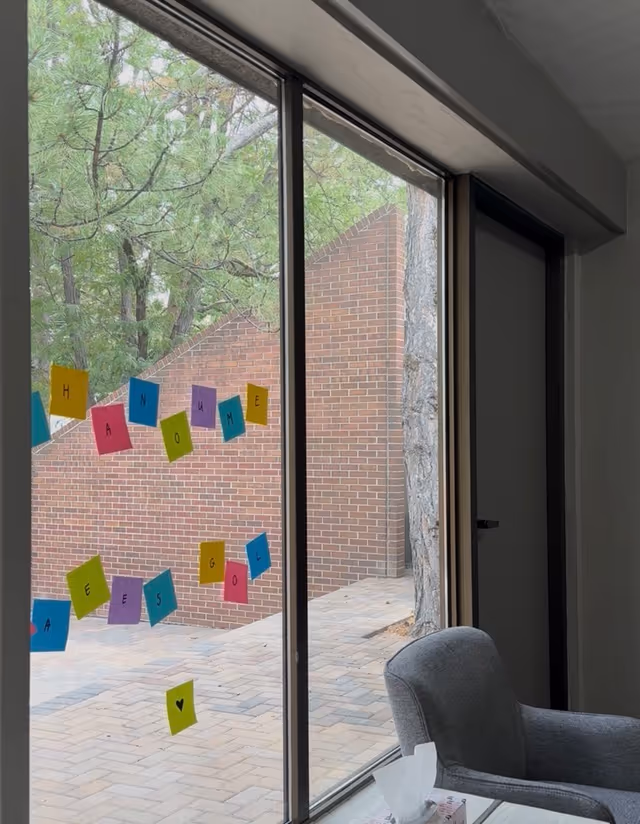 Interior lounge area with large windows, a gray chair, and colorful sticky notes on glass.