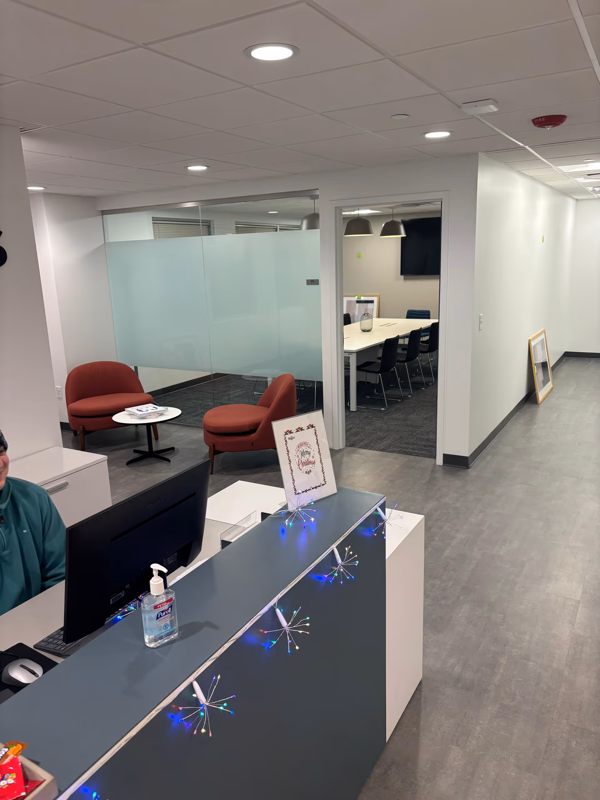 Reception desk with sanitizer; glass-walled conference room and waiting area inside facility.