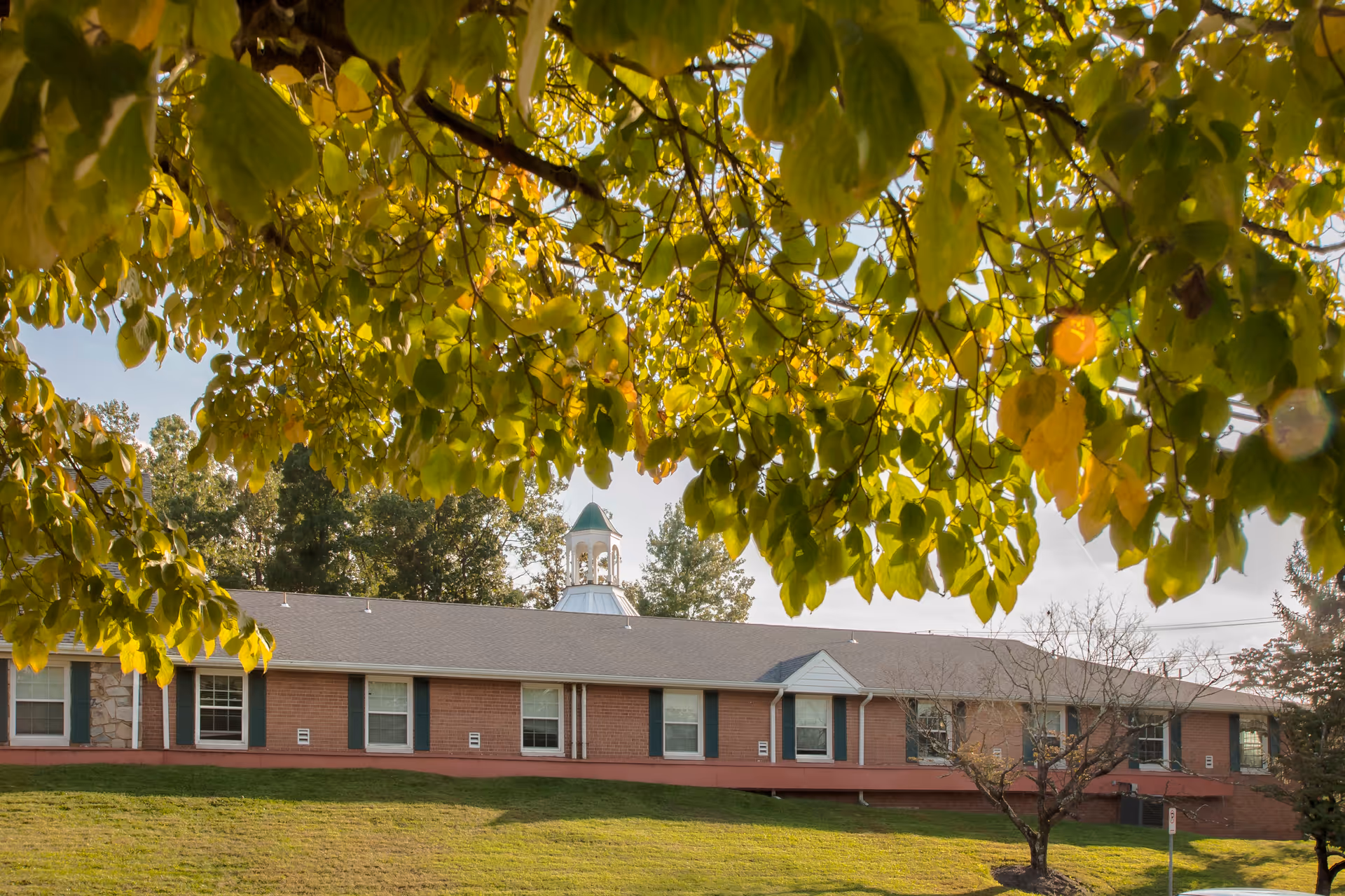 Front view of a single-story brick senior living building with green lawn and trees.