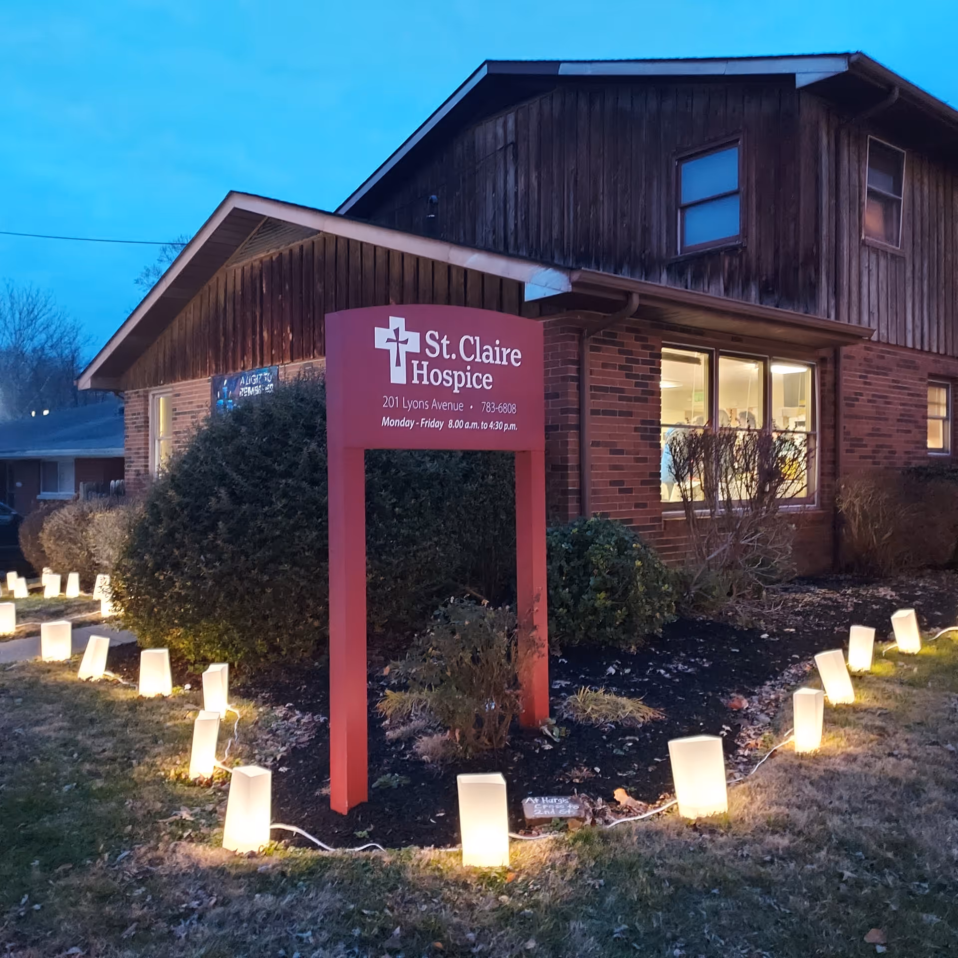 Exterior view of St. Claire Hospice building with a red sign and pathway lights.