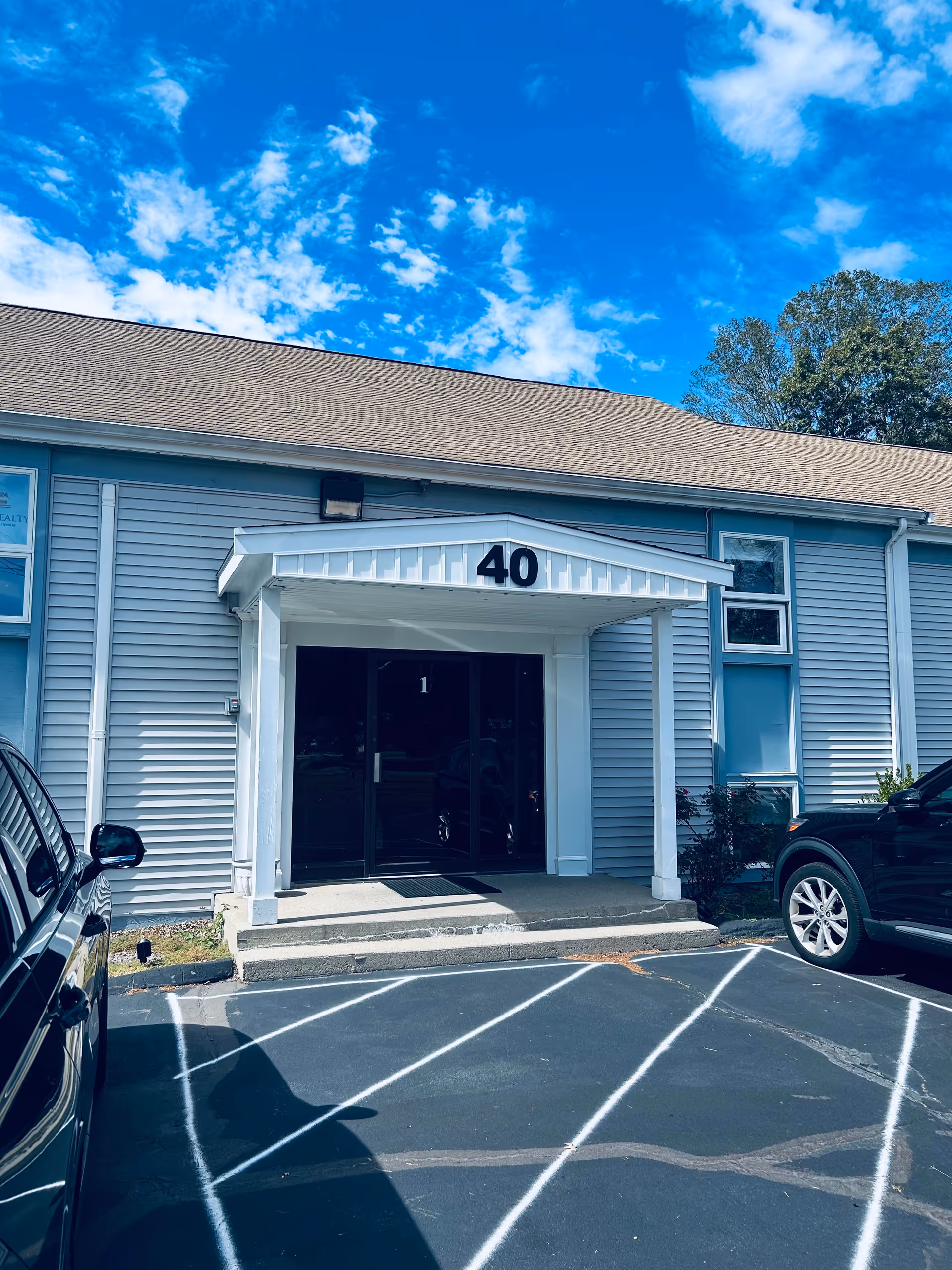Carelicity facility entrance with white canopy, blue siding, and cars in the front parking area.