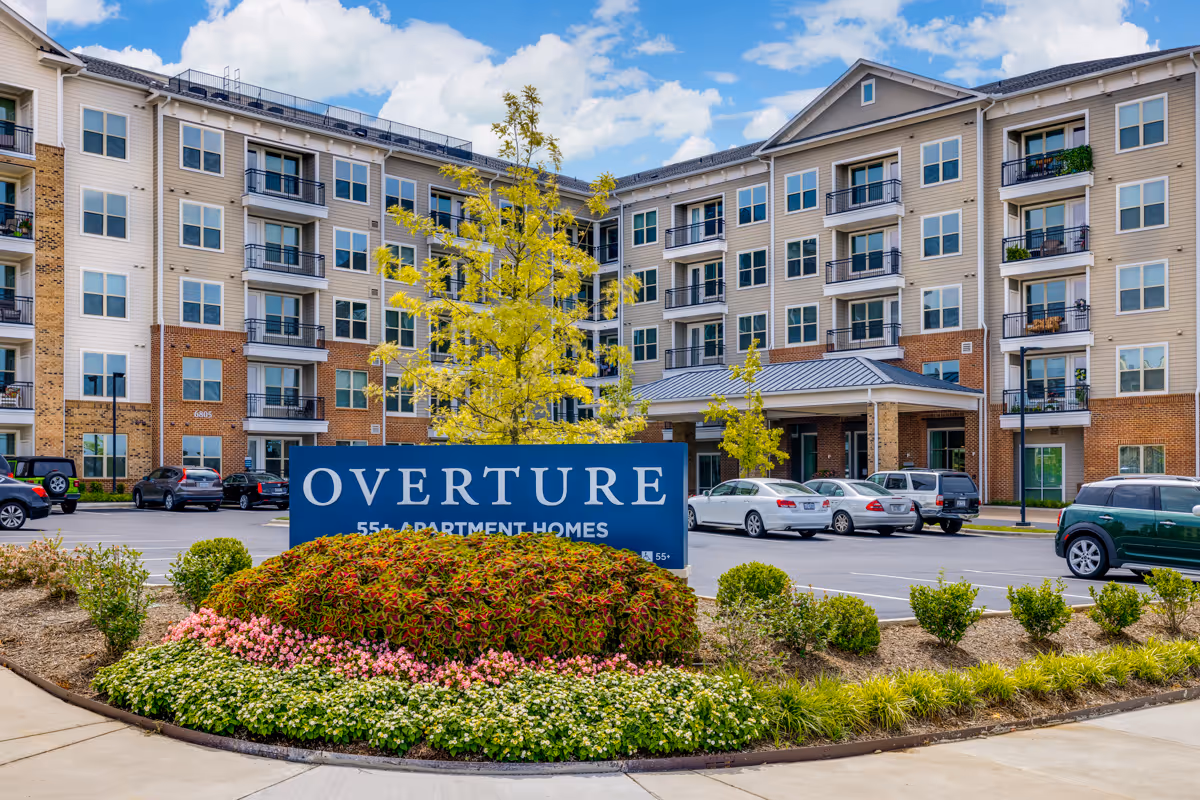 Multi-story beige apartment building with balconies, front sign 'Overture,' and landscaped entrance.