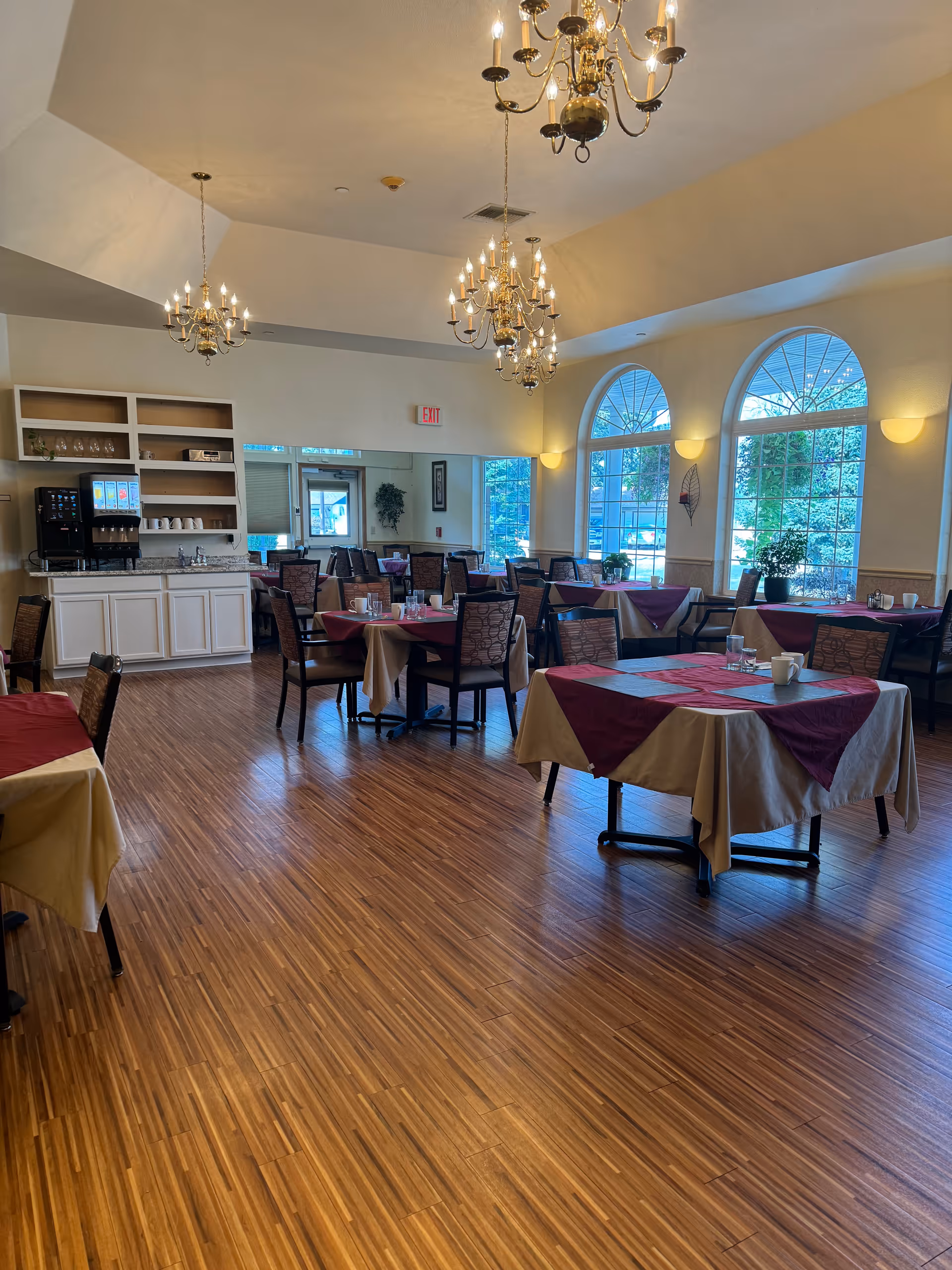 Interior dining room at Colonial Court senior living facility with tables and chandeliers.