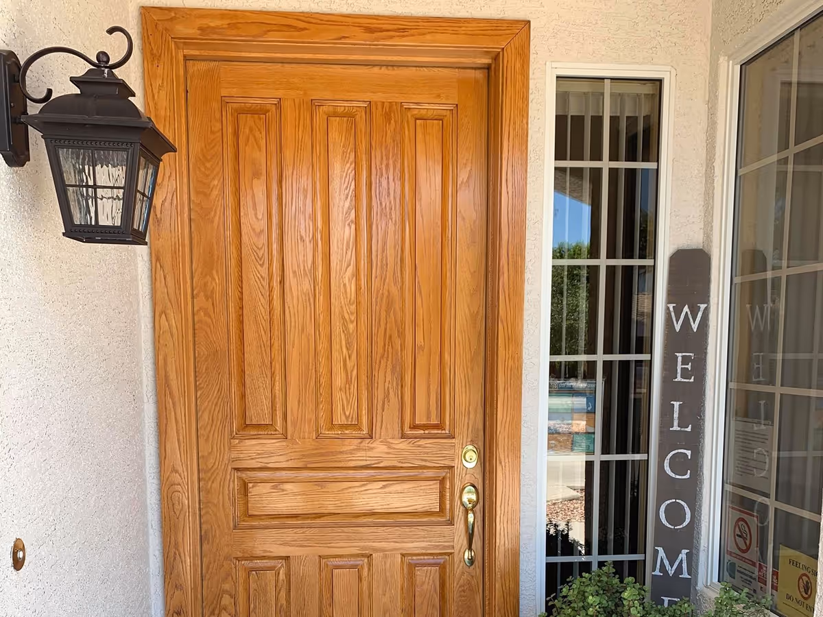 Wooden front door with a lantern light and a welcome sign beside glass windows.