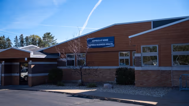 Exterior view of Aspirus At Home facility with signage and landscaping.