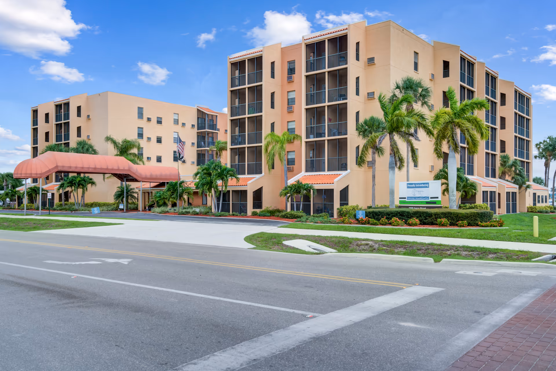 Exterior view of a tan senior living building with palm trees and a pink entrance canopy.