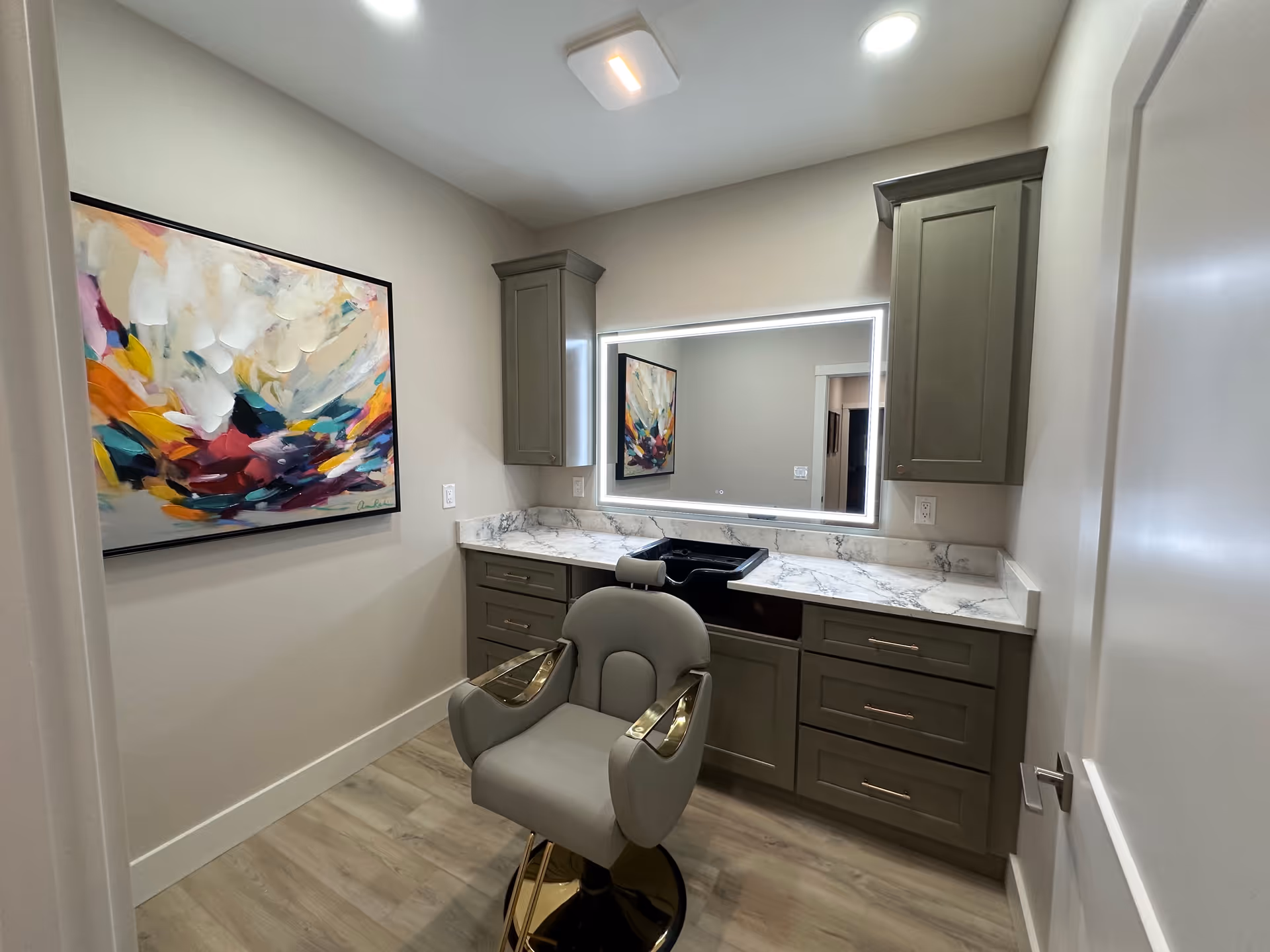 Modern bathroom vanity with gray cabinets, marble counter, illuminated mirror, and chair.
