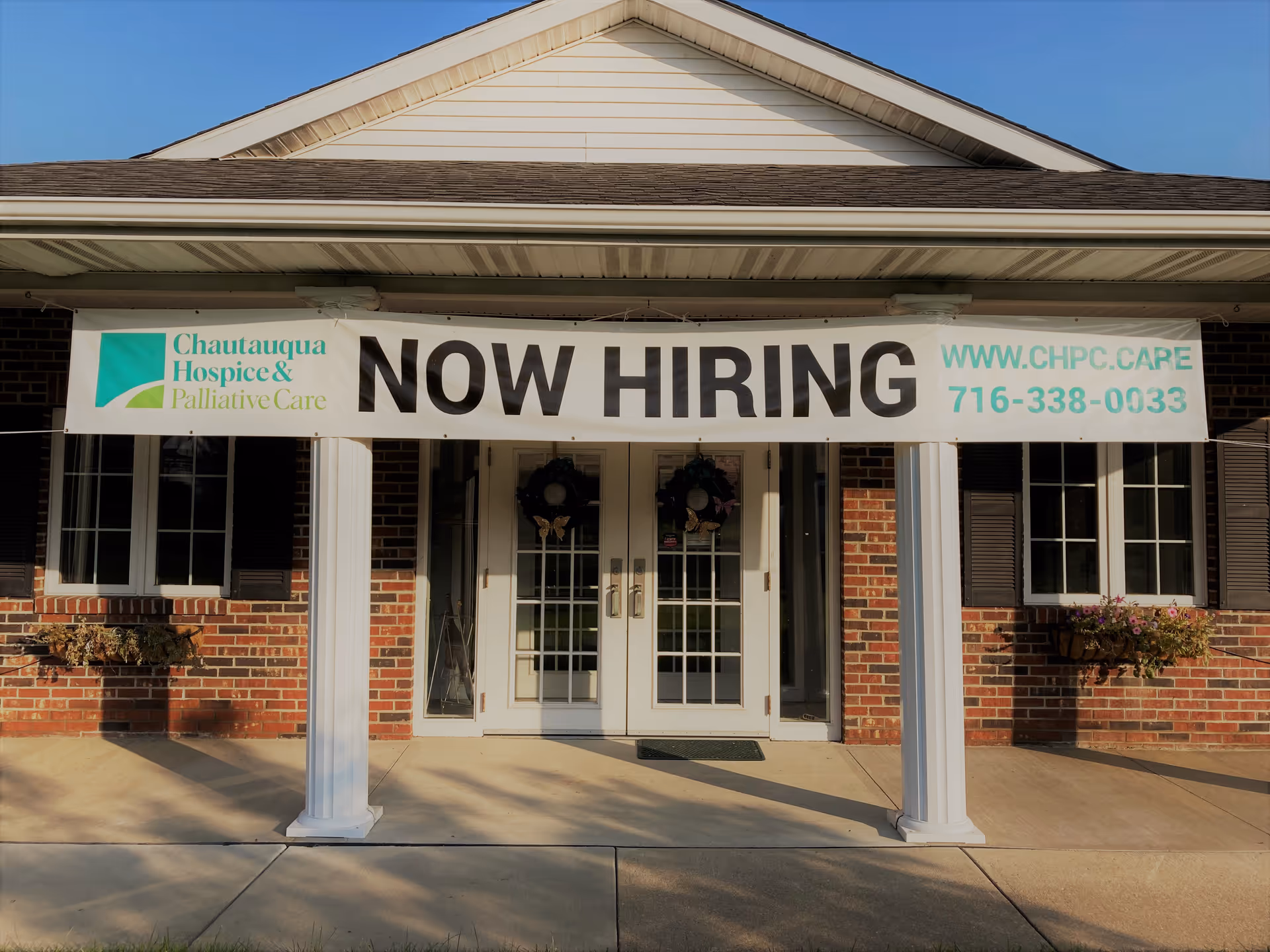 Brick building exterior with a NOW HIRING banner across the front entrance.