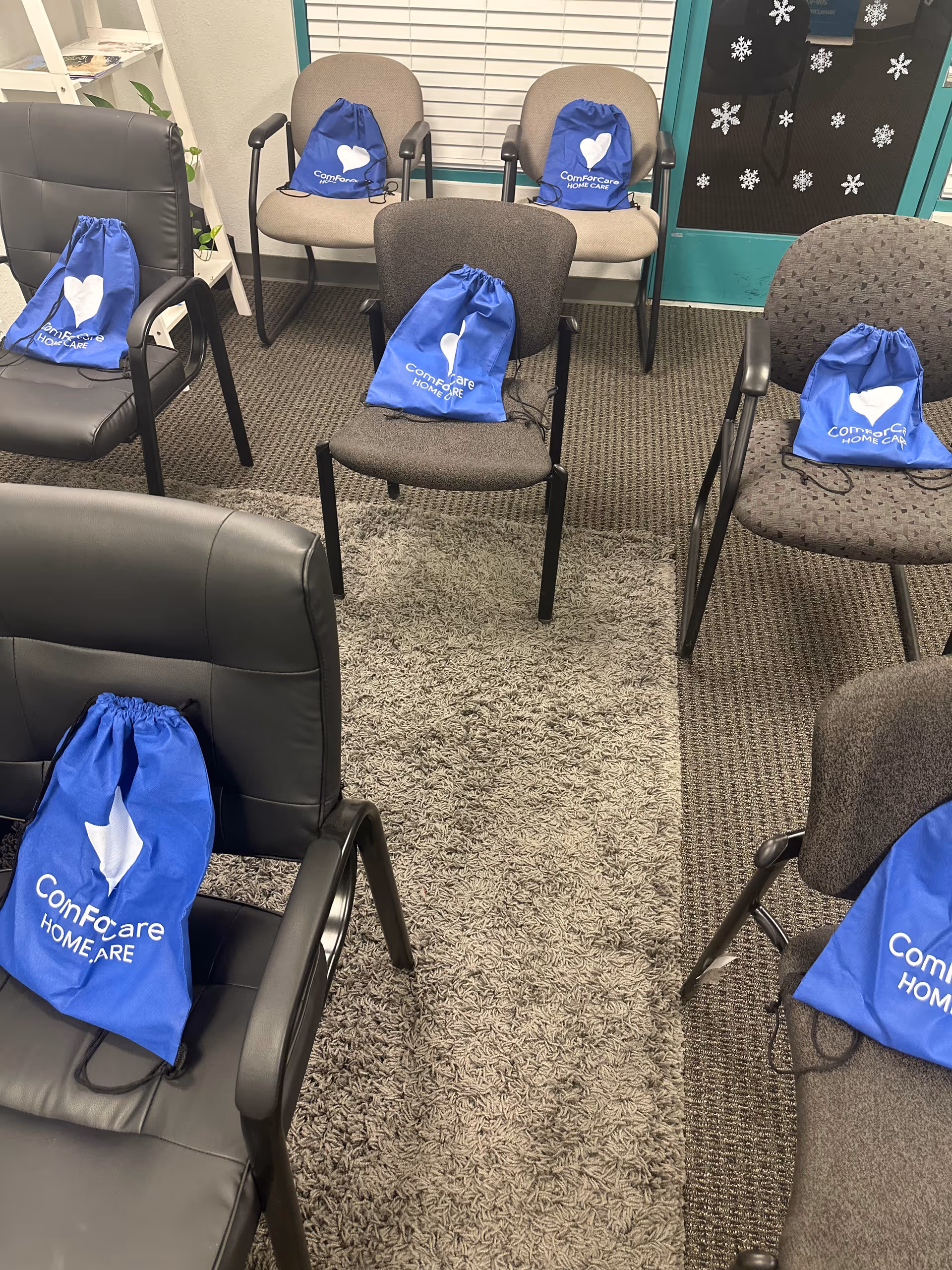 Indoor waiting area with several chairs and blue ComForCare bags on them.