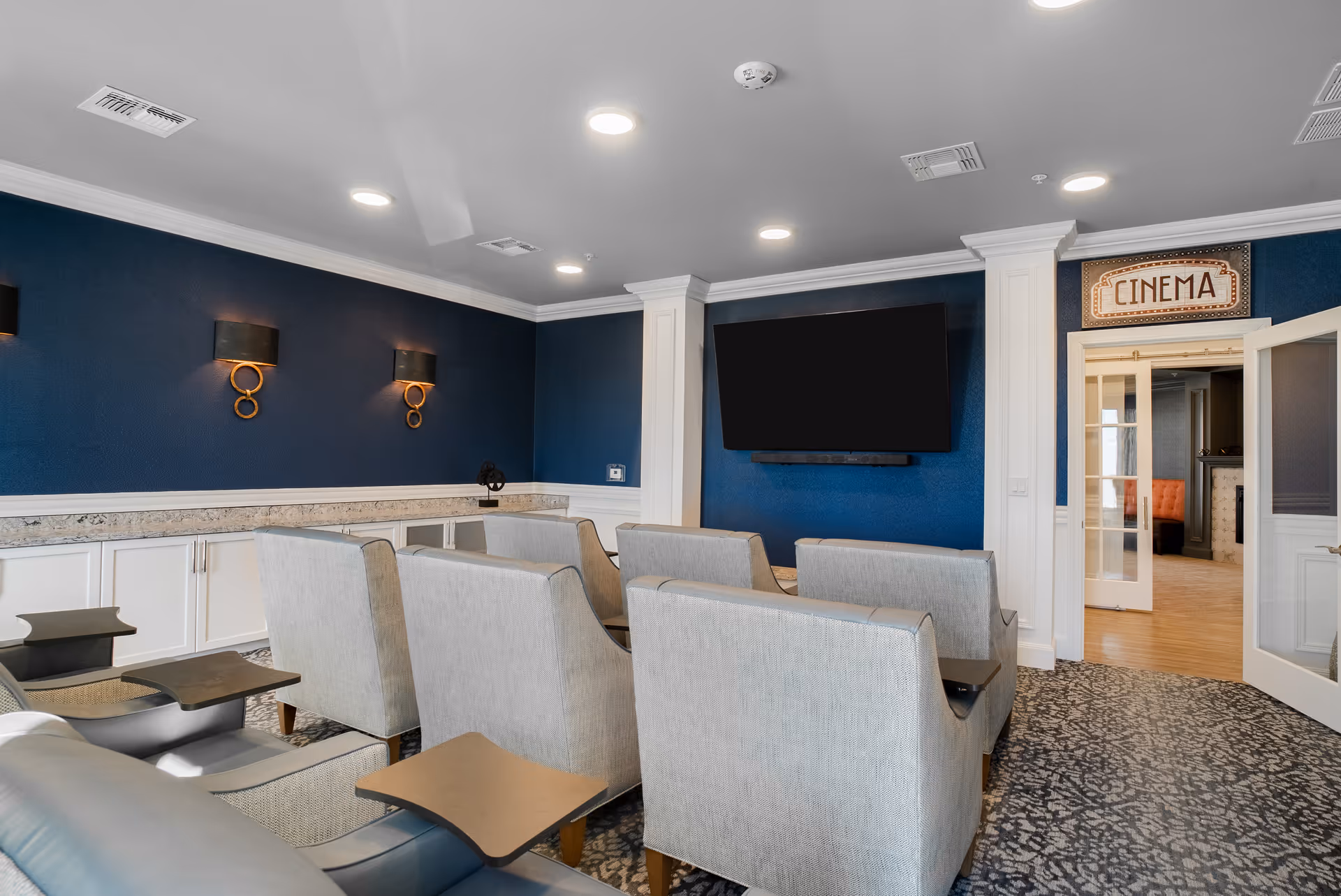 Senior living lounge with blue walls, theater seating, a wall TV, and a CINEMA doorway.