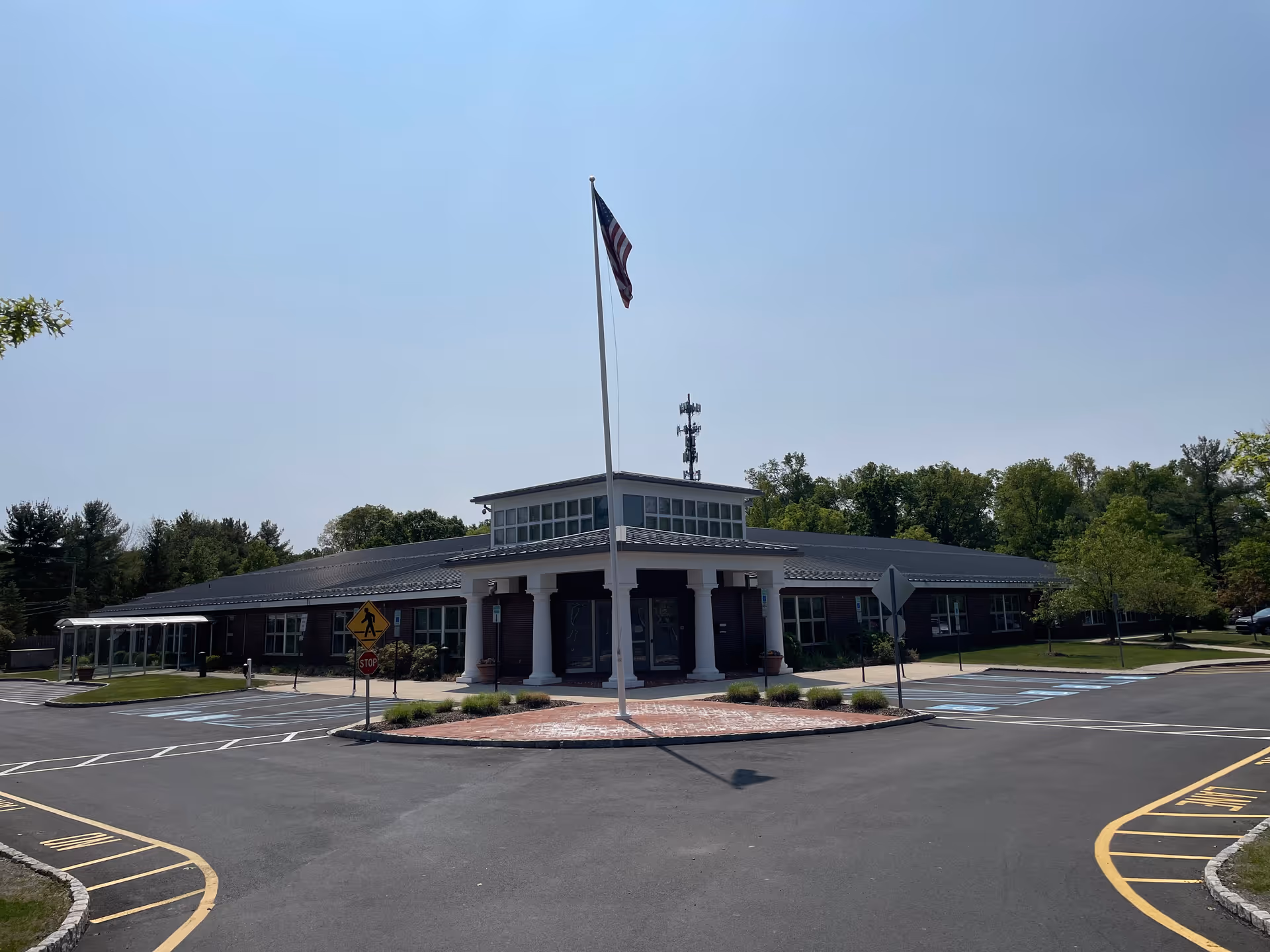 Exterior view of a single-story senior living facility with columns, flagpole, and parking.