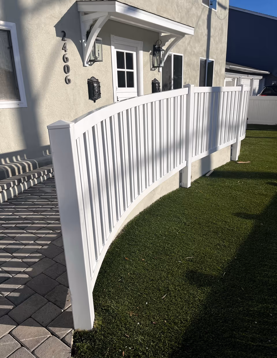 White curved fence along a front yard leads to a beige building entrance with steps.