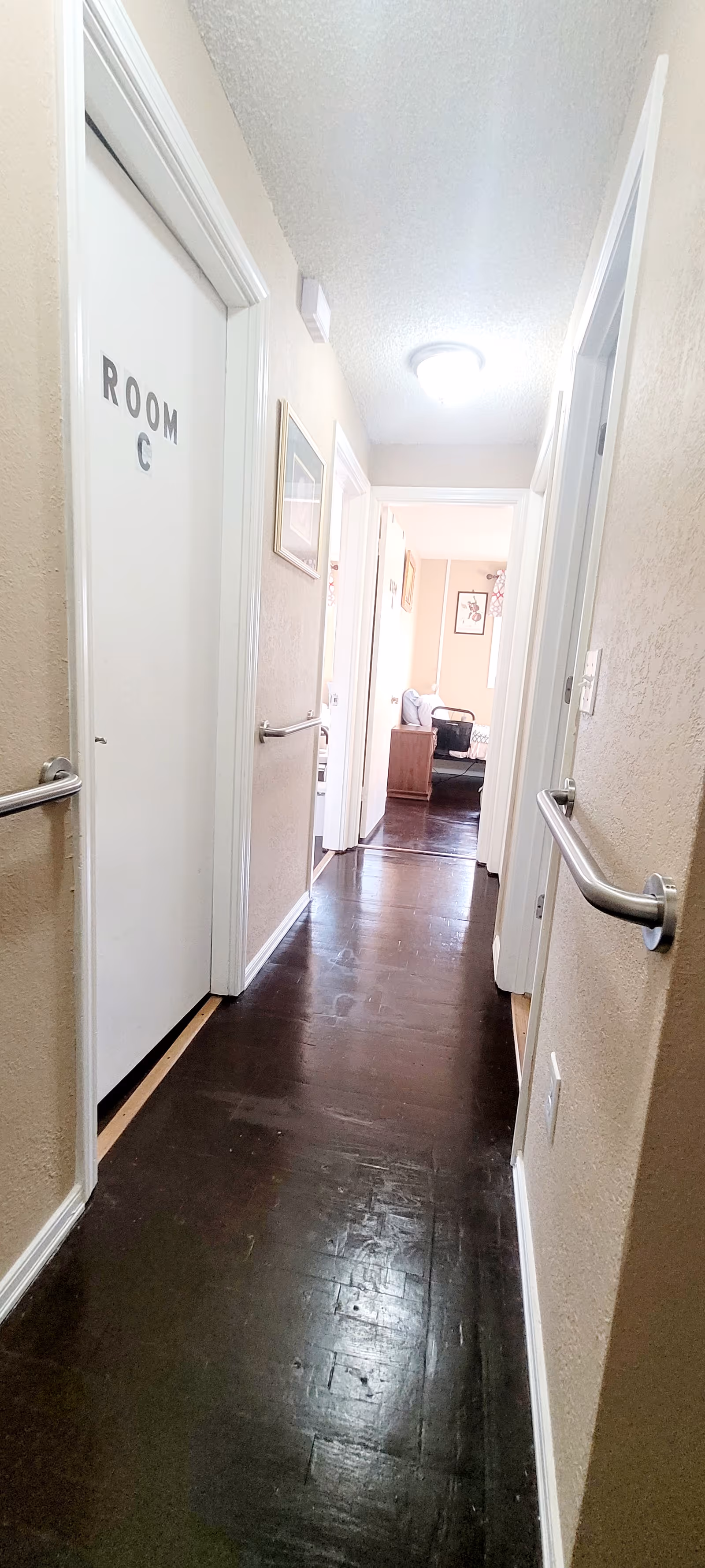 Narrow interior hallway of a senior living facility with doors, handrails, and a distant room.