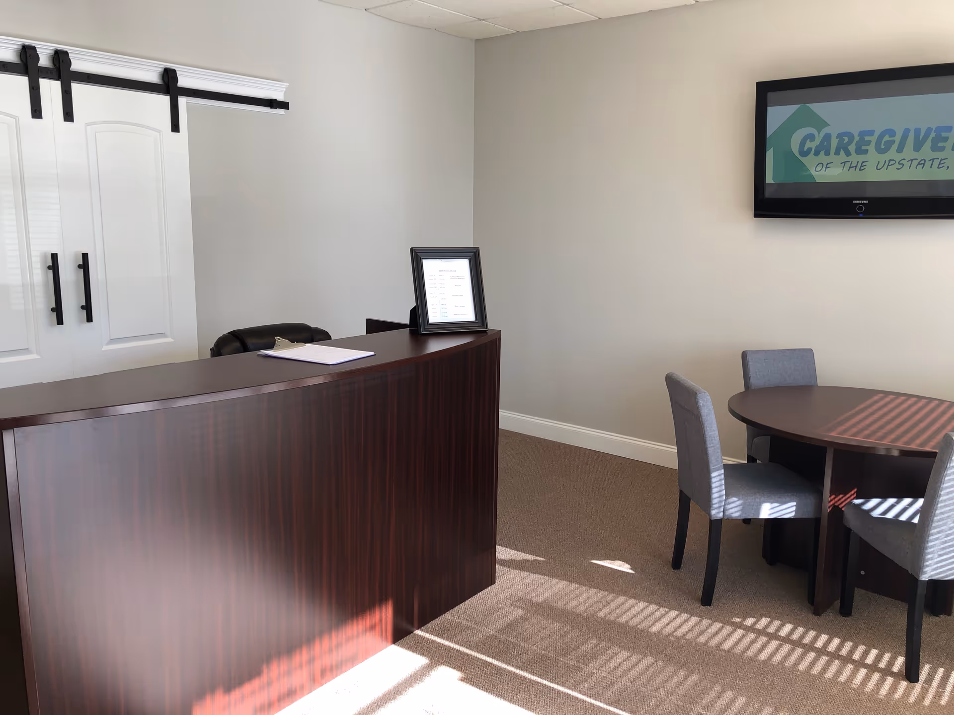Reception area with dark wood desk, seating, cabinets, and a wall-mounted screen.