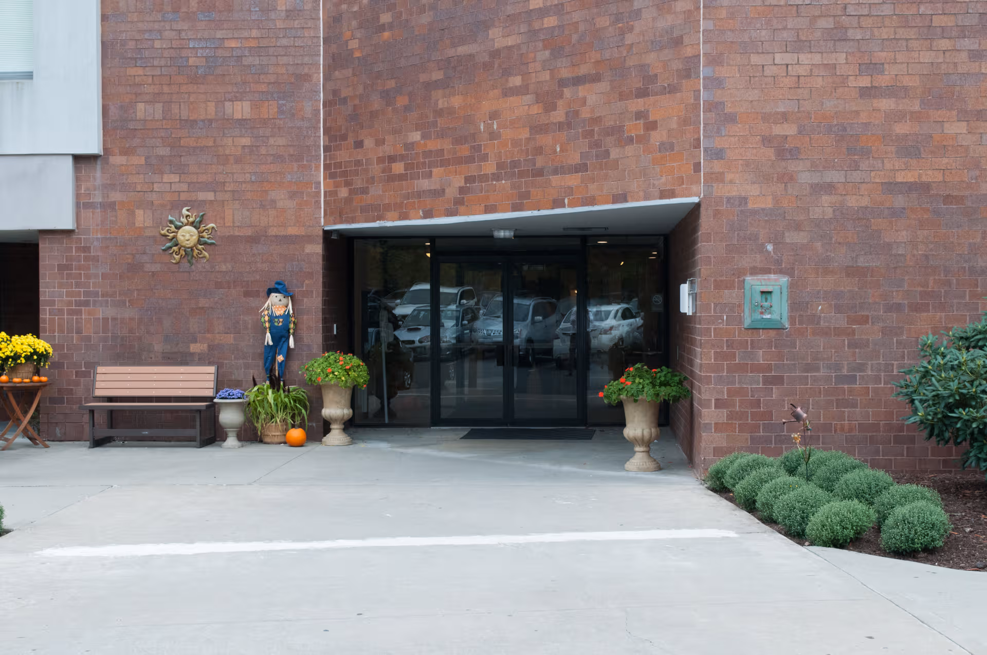 Brick building entrance with glass doors, bench, and potted plants outside Chelsea Place Care Center.