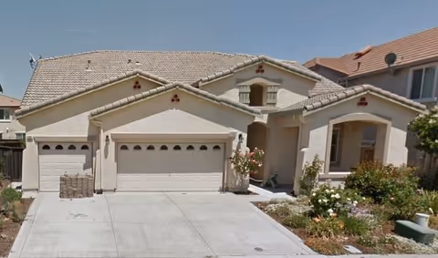 Beige suburban house with a three-car garage and landscaped front yard.