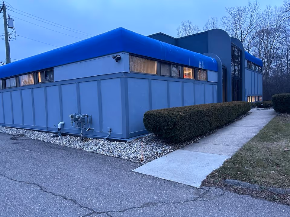 Blue exterior building with a walkway, manicured hedges, and a curved roof along the side.