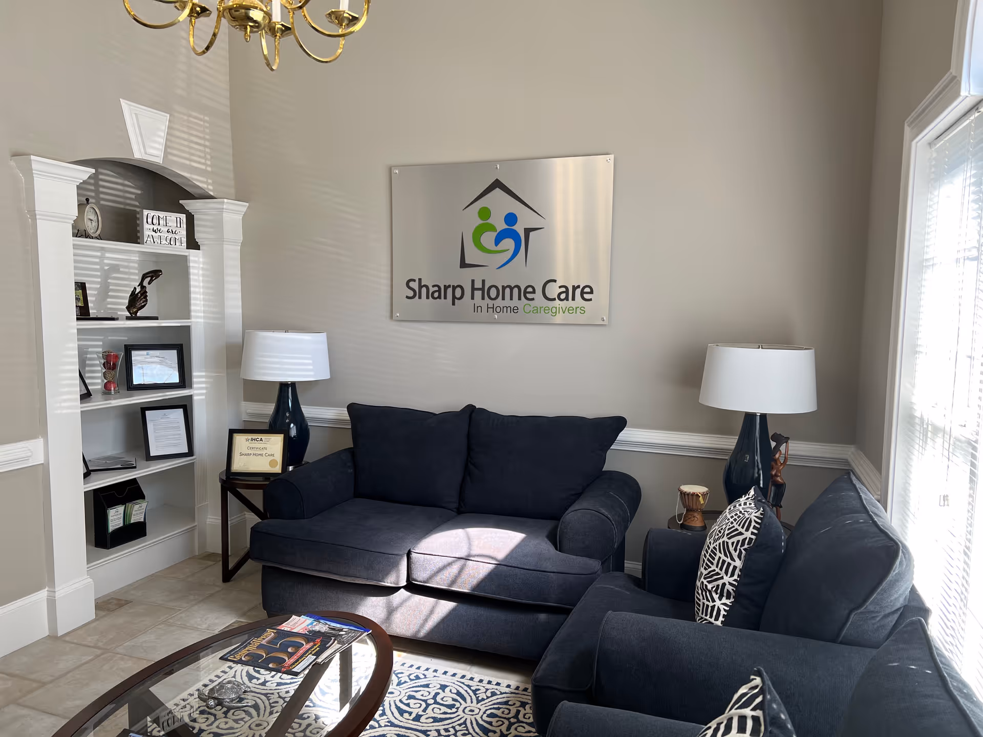 Cozy facility living room with navy sofas, lamps, and Sharp Home Care sign on wall.