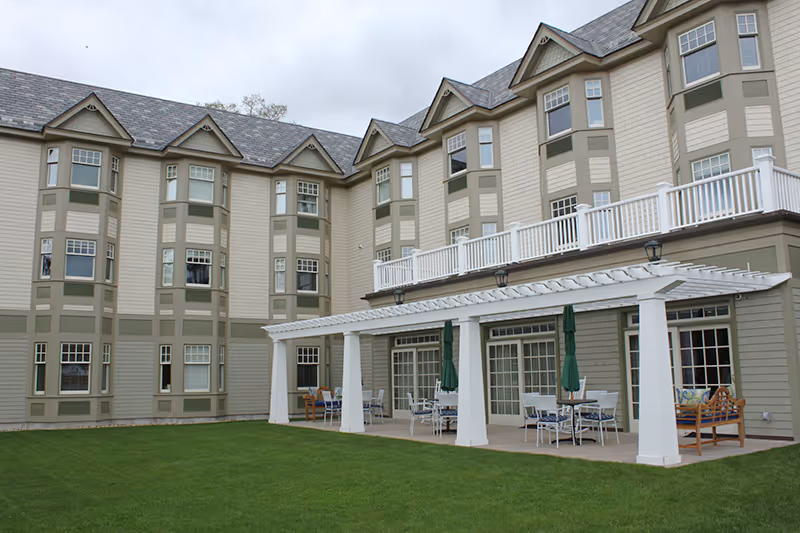 Exterior view of Blaire House of Milford Assisted Living with a white pergola patio and lawn