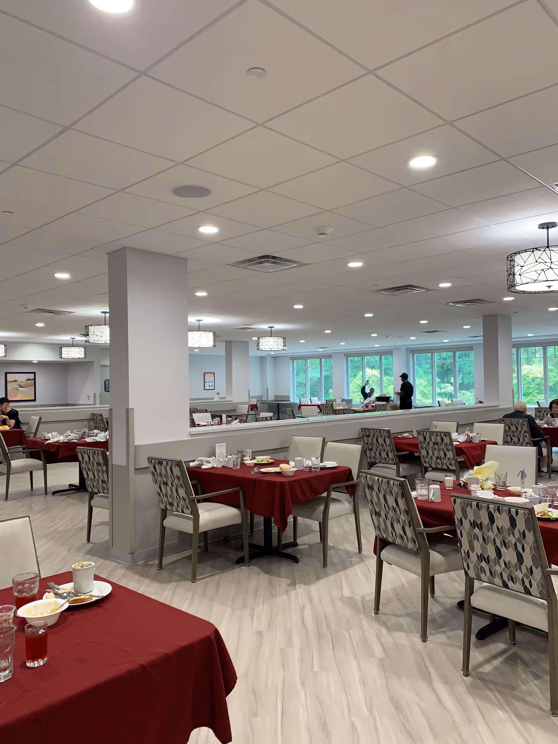 Senior dining room with red tablecloths, arranged tables, and large windows.
