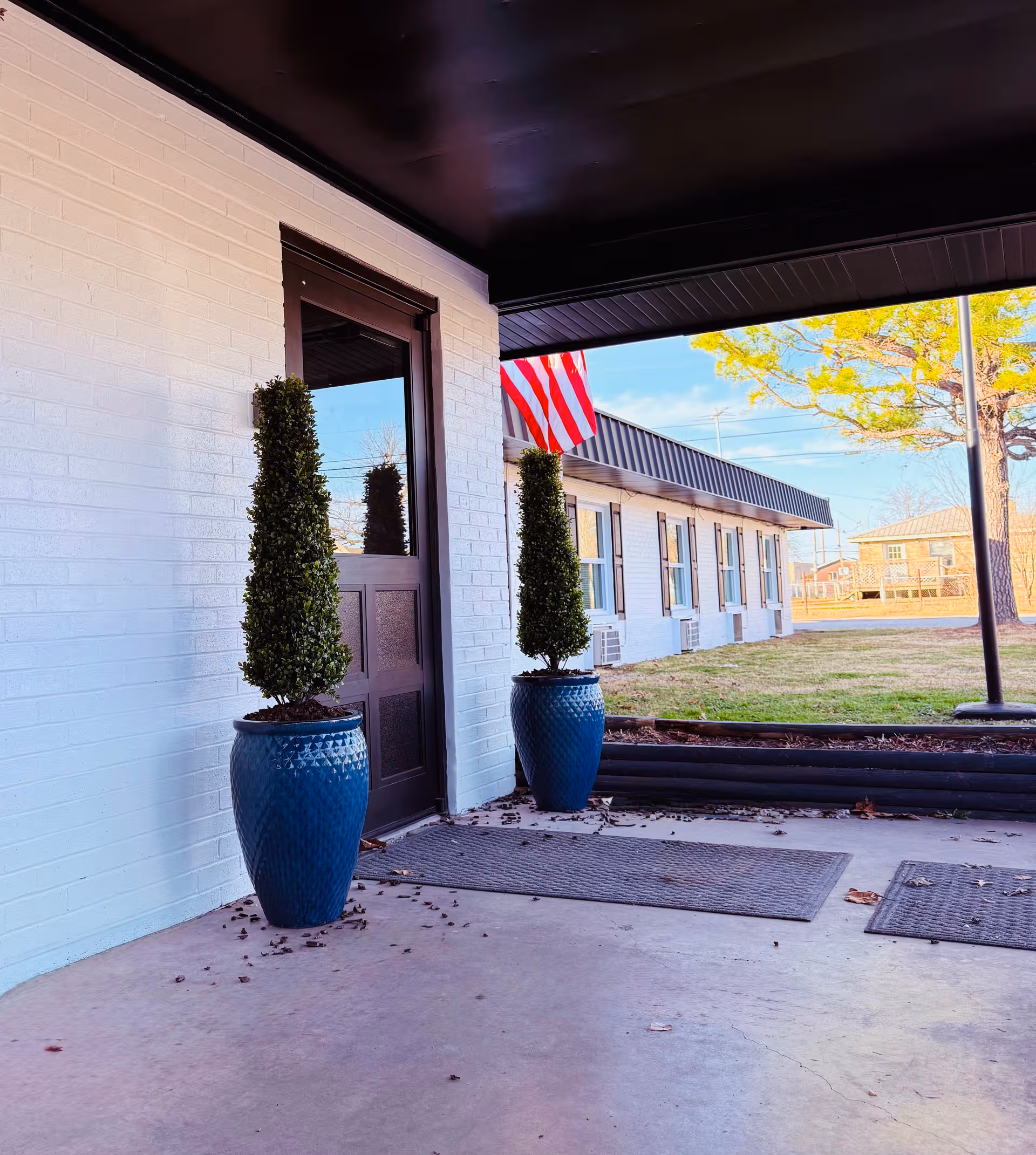 White brick building entrance with two blue pots and an American flag.