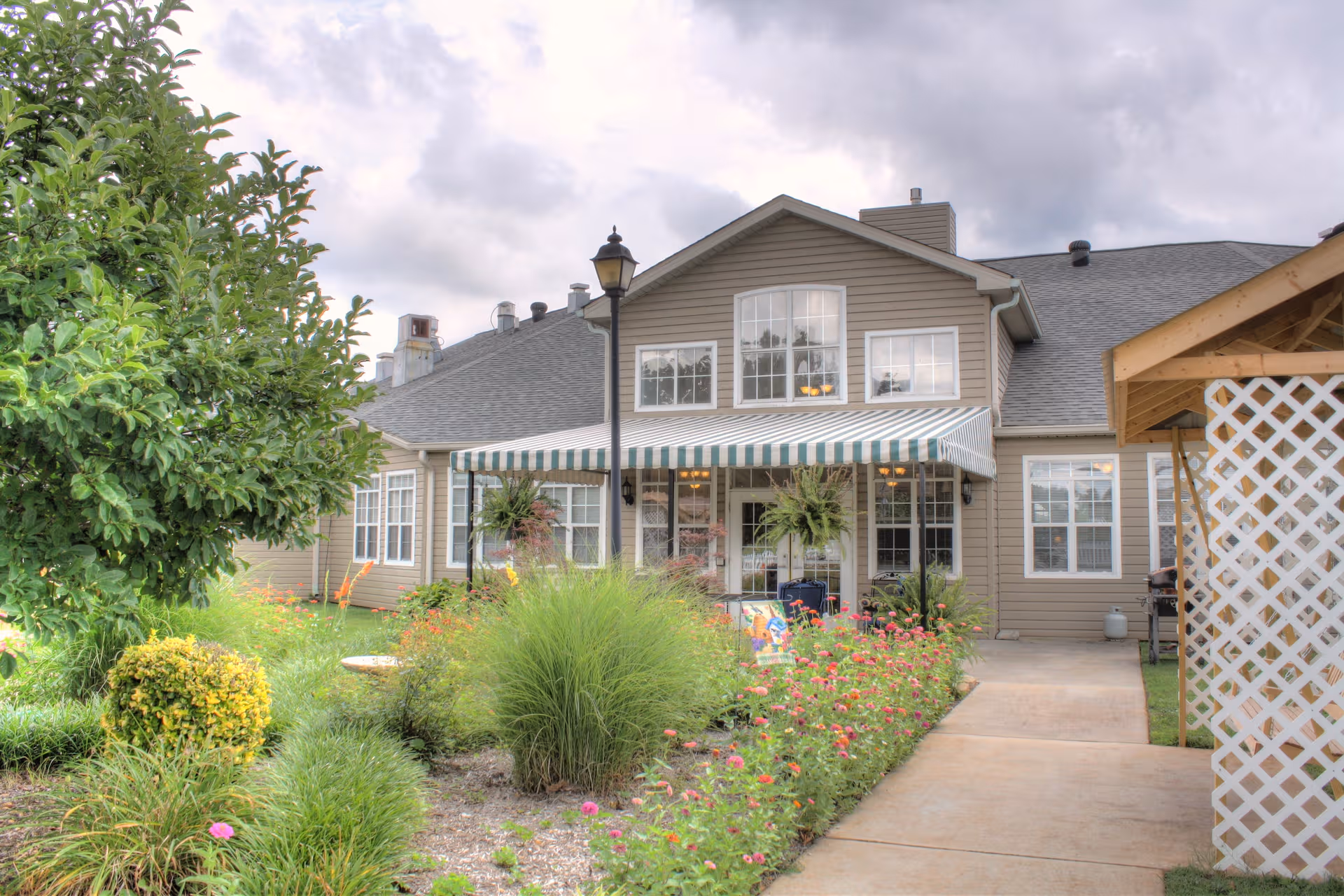 Gray two-story senior living facility with striped awning, garden, and paved walkway.