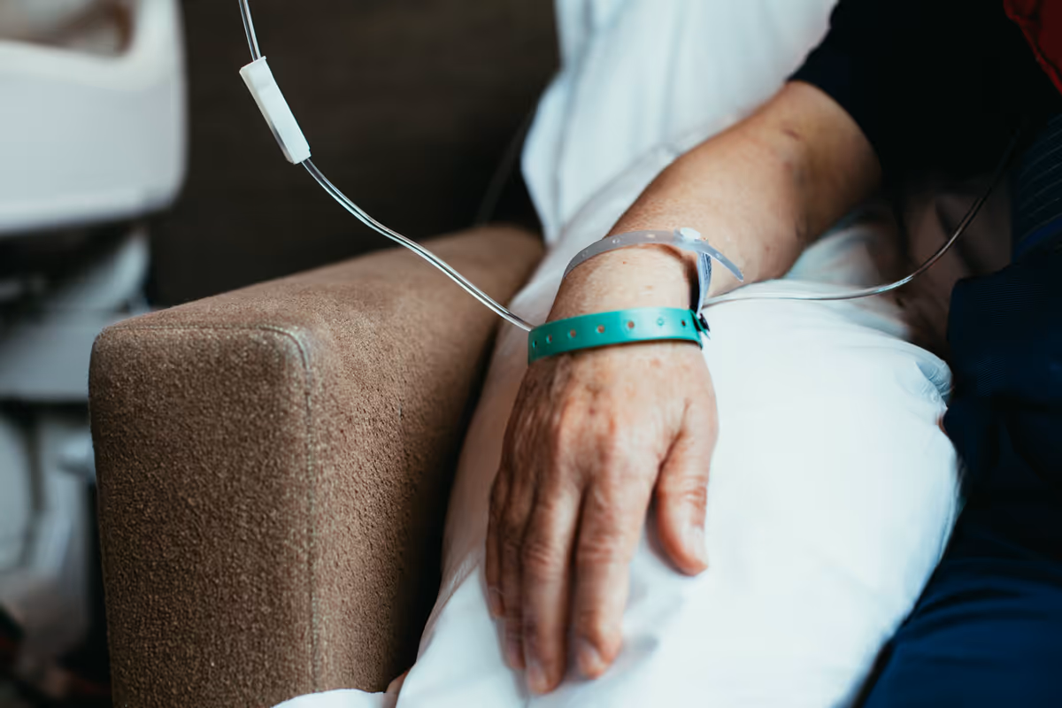 Close-up of an elderly person's arm with an IV line and hospital bracelet.