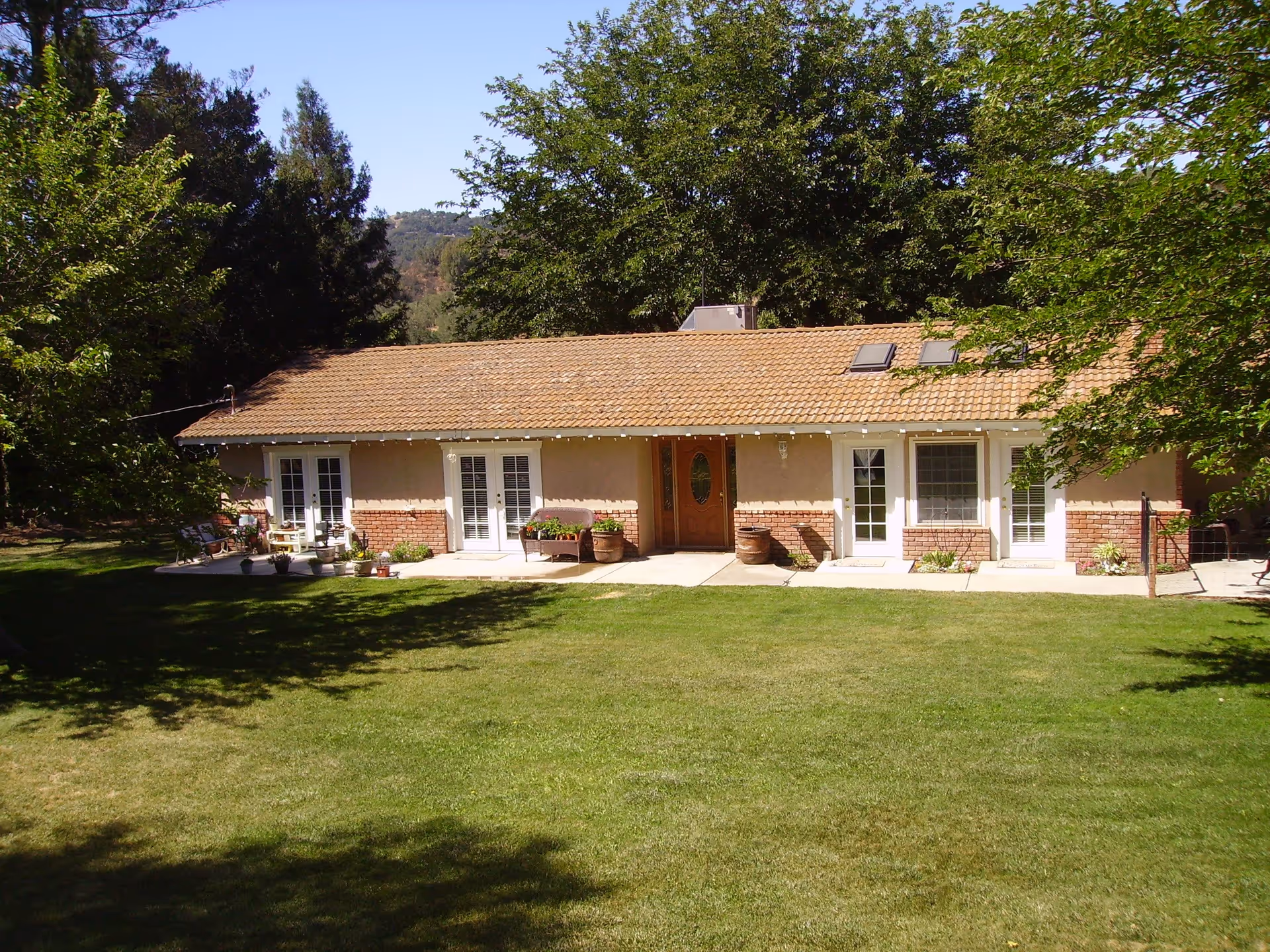 Single-story ranch-style building with a tiled roof, front patio doors and planters, and a large grassy lawn surrounded by trees.