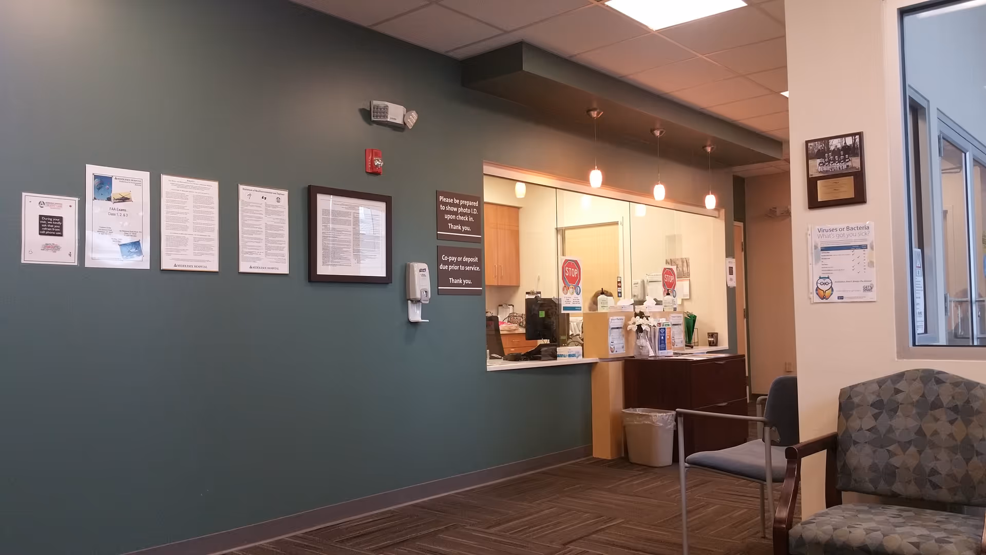 Lobby area with reception window, teal wall, posted notices, and seating.