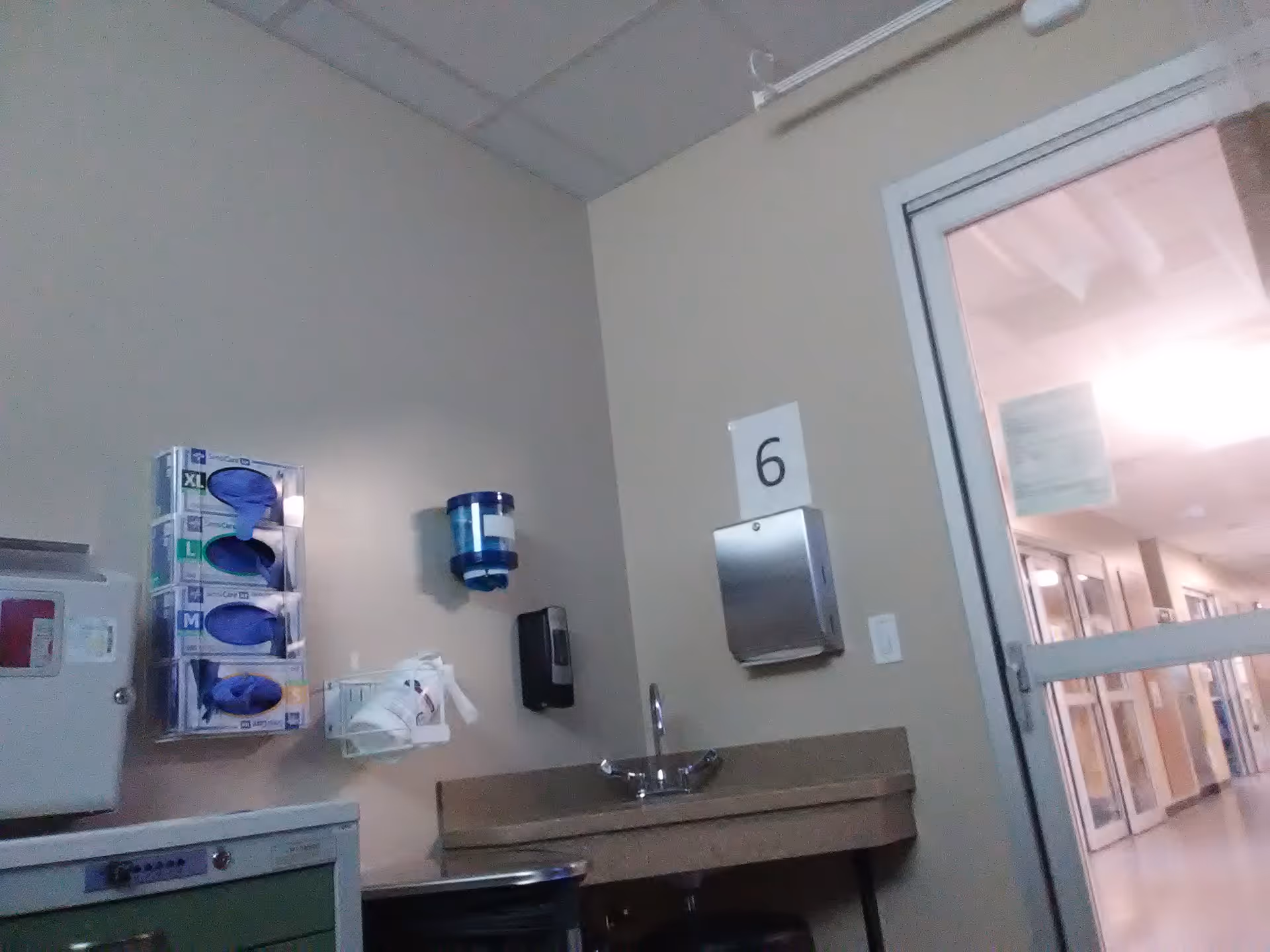 Interior hospital-like hallway with sink, glove packs, sanitizer, and a numbered door.