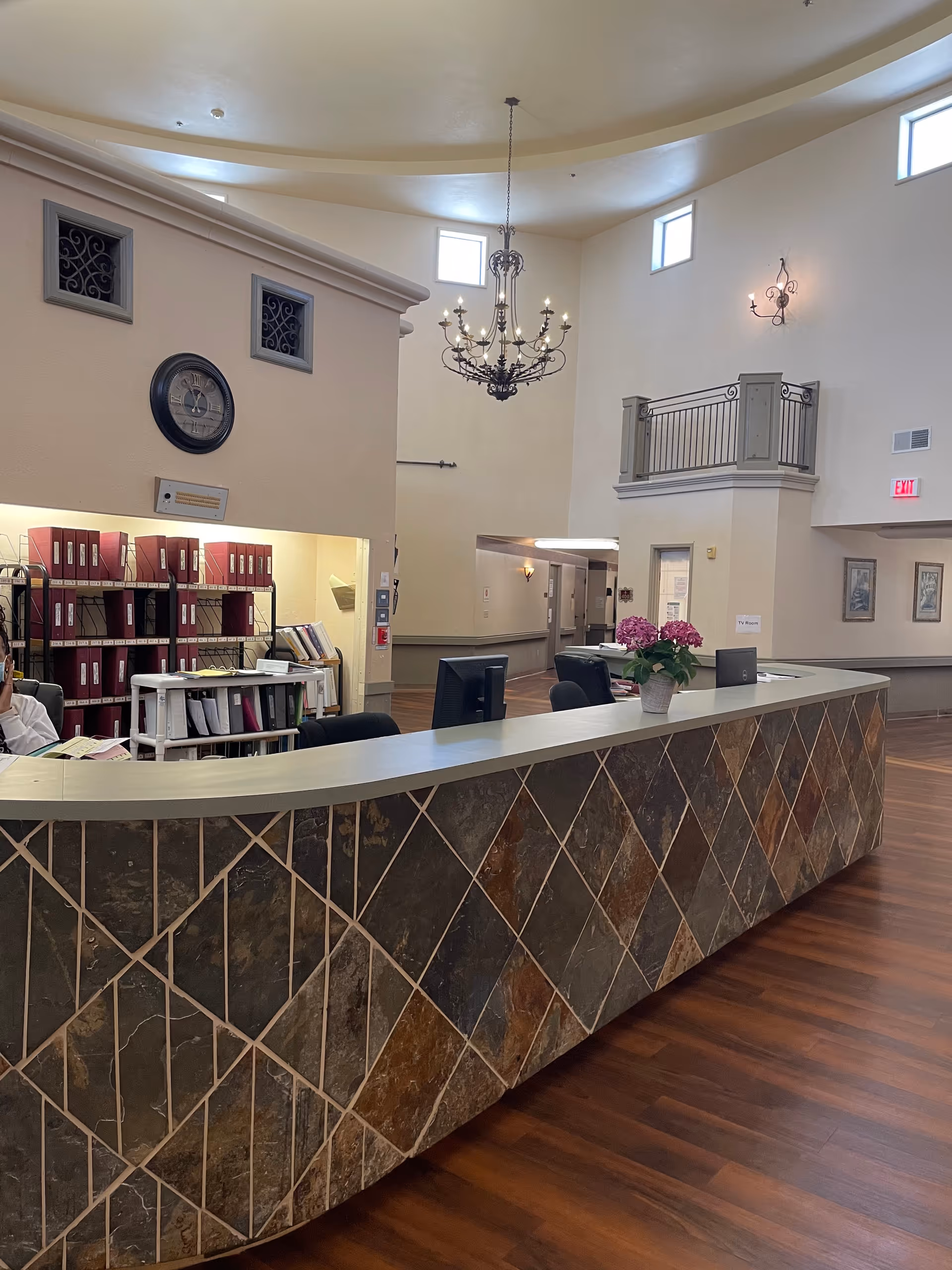 Curved tile-front reception desk in a bright, high-ceilinged senior living facility lobby.