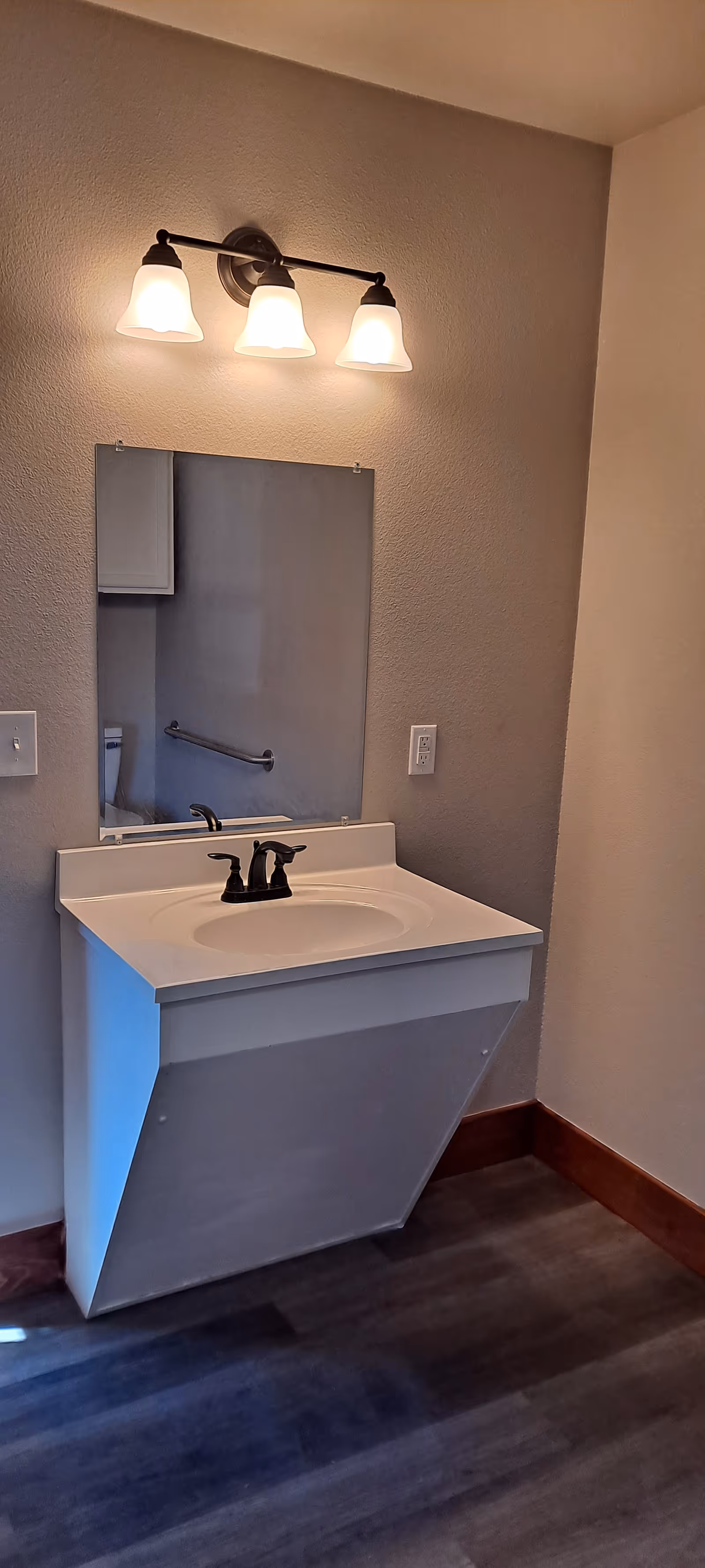 Bathroom vanity with sink, mirror, and three-light fixture in a senior living facility.
