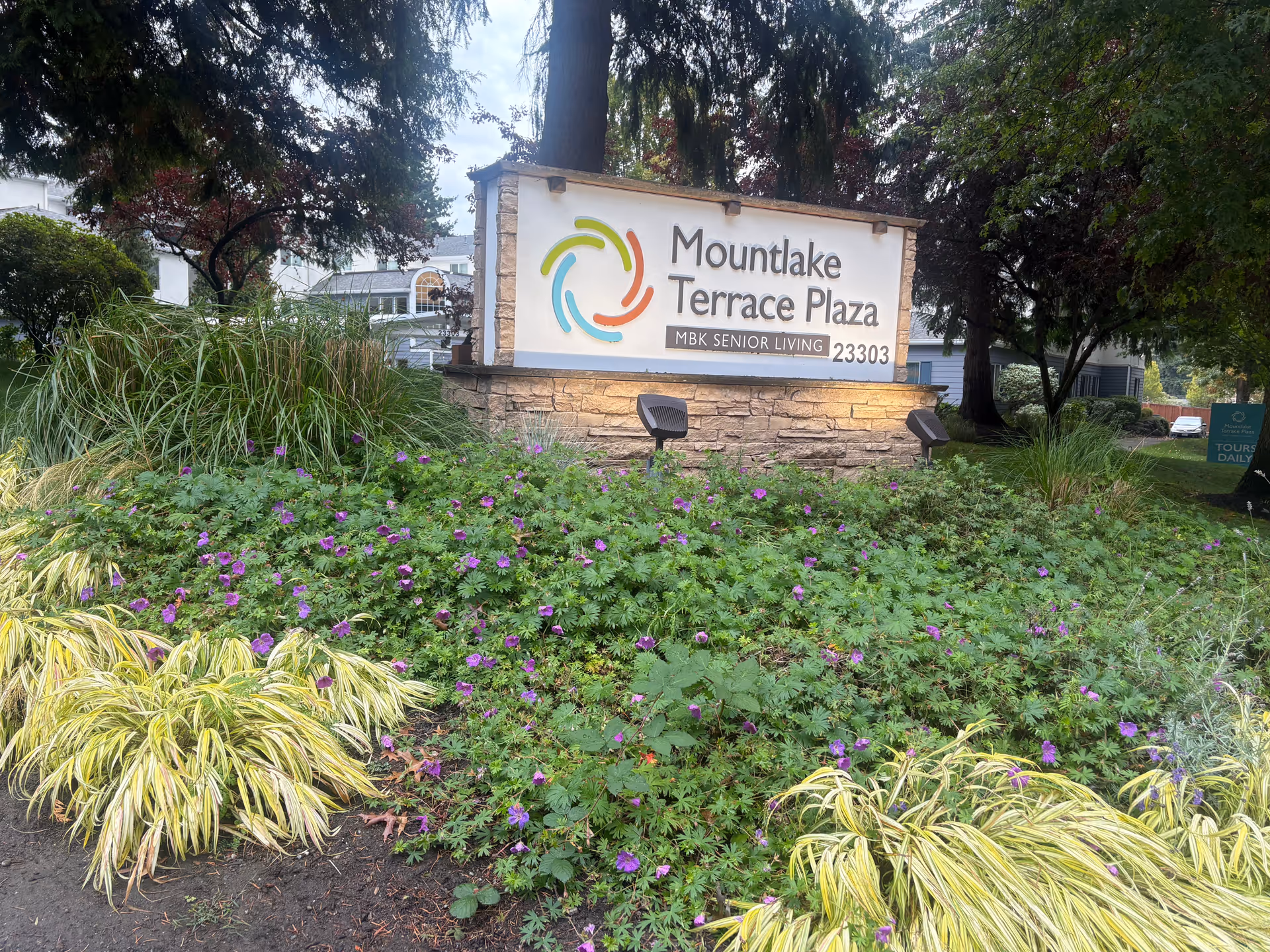 Stone sign reads Mountlake Terrace Plaza with colorful circular logo, surrounded by landscaped bushes.