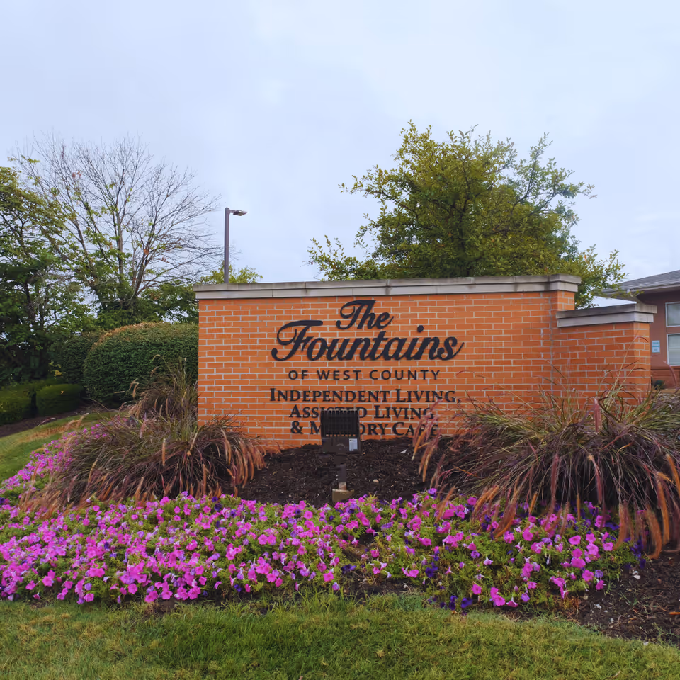Exterior view of The Fountains of West County entrance sign with colorful flowers.
