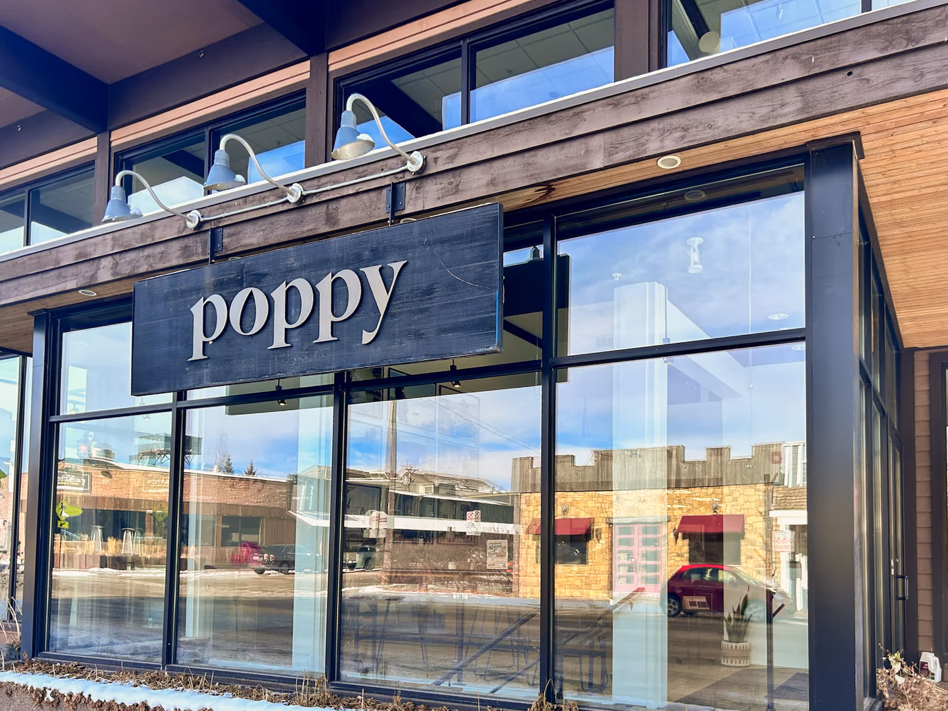 Glass-front storefront with a large 'poppy' sign and reflected street view.