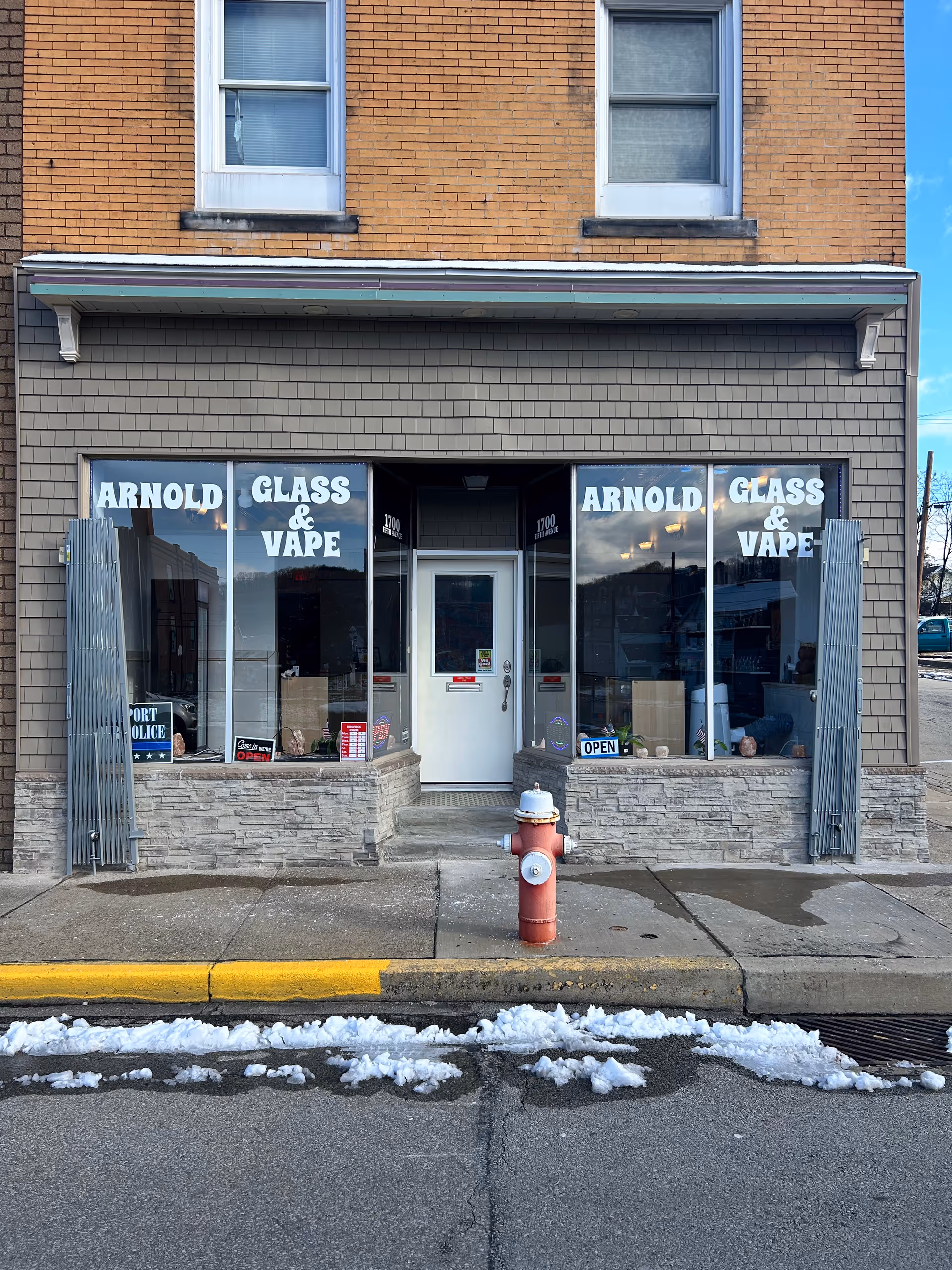 Brick storefront with large glass windows advertising Arnold Glass & Vape and a central white door.