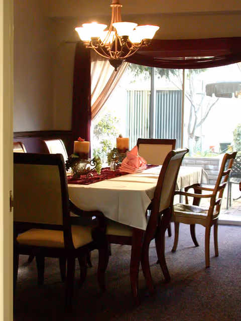 Dining room with a table set with candles and folded napkins under a chandelier and sliding glass doors to a patio.