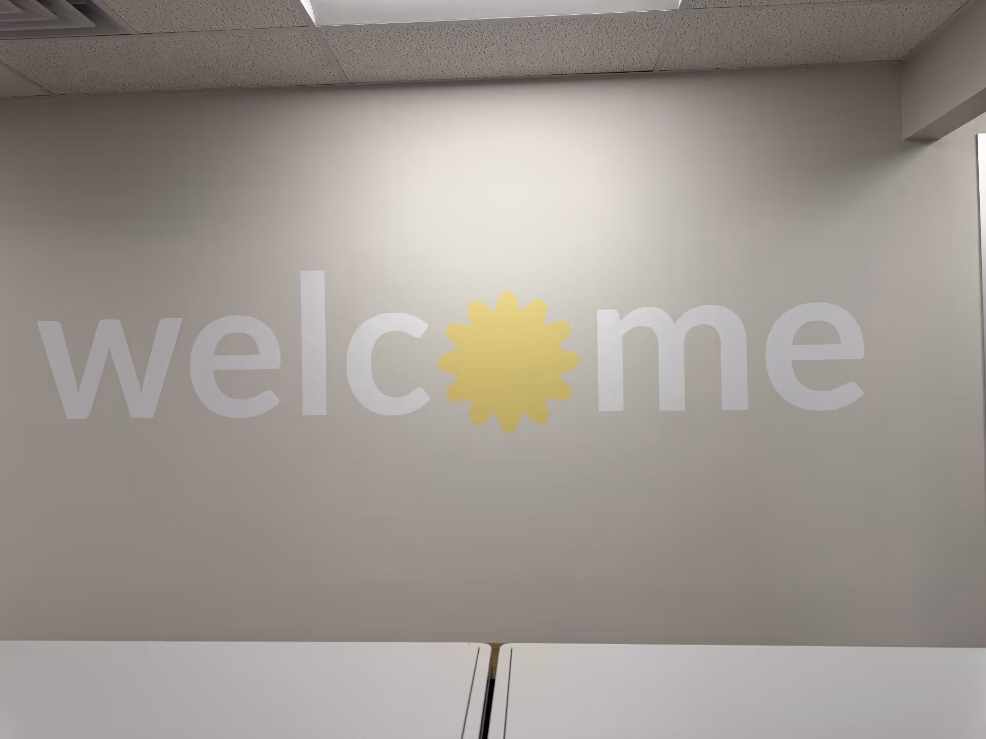 Gray interior wall with large welcome lettering and a yellow sun replacing the O.