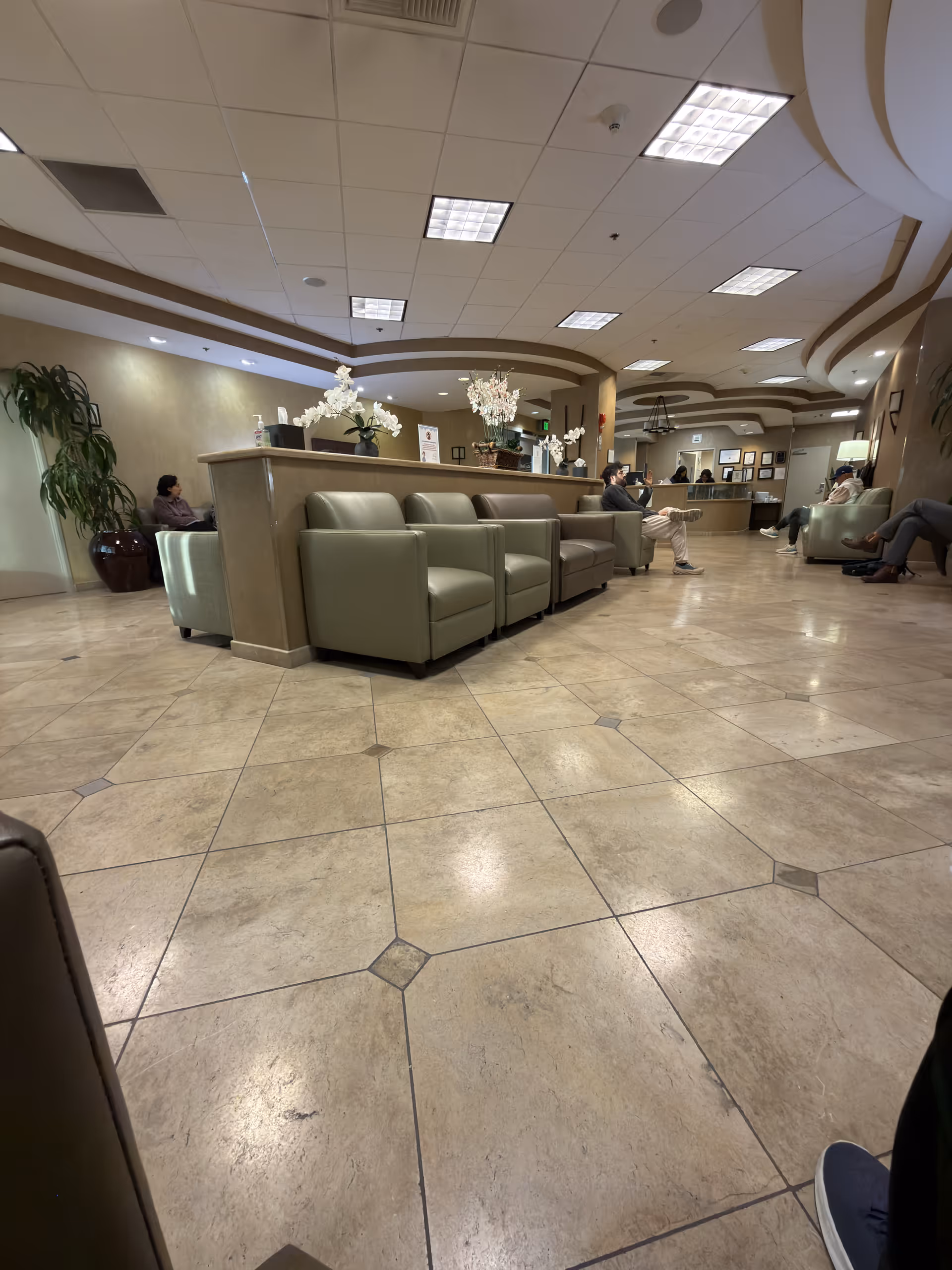 A spacious hospital-like lobby with beige tile floor, curved reception desk, and seating.