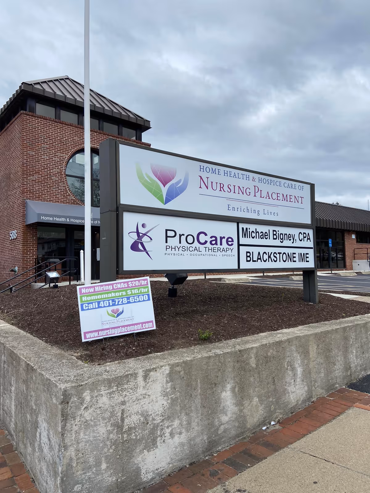 Exterior view of a nursing placement facility with a large front signboard beside a brick building.